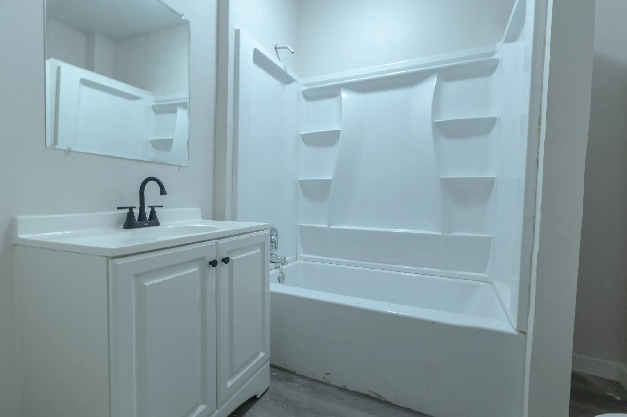 Bathroom featuring a white vanity with panel-front cabinetry, a matte black faucet, and a coordinating framed mirror