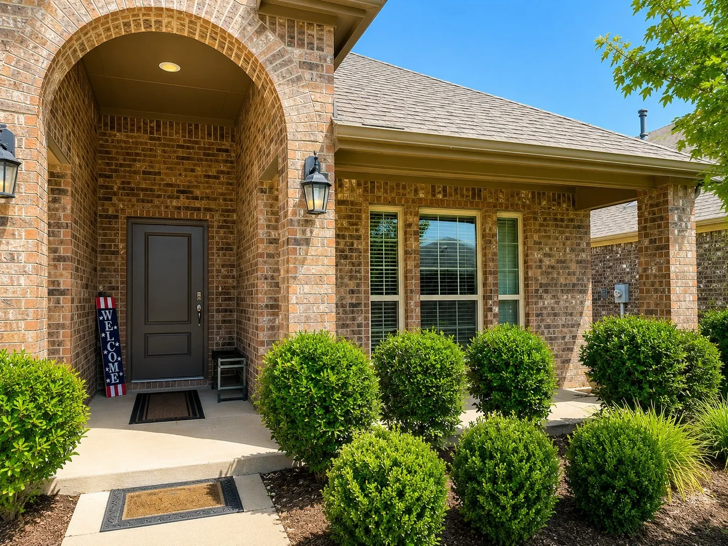 Brick exterior featuring an arched entryway, covered porch, dark paneled front door, and exterior lighting fixtures