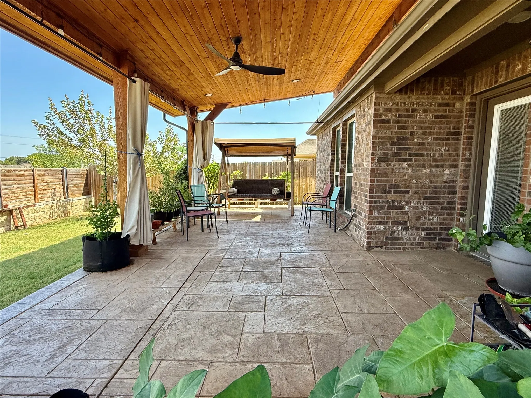 Expansive covered patio featuring a wood-panel ceiling with a ceiling fan, stamped concrete flooring, and privacy curtains