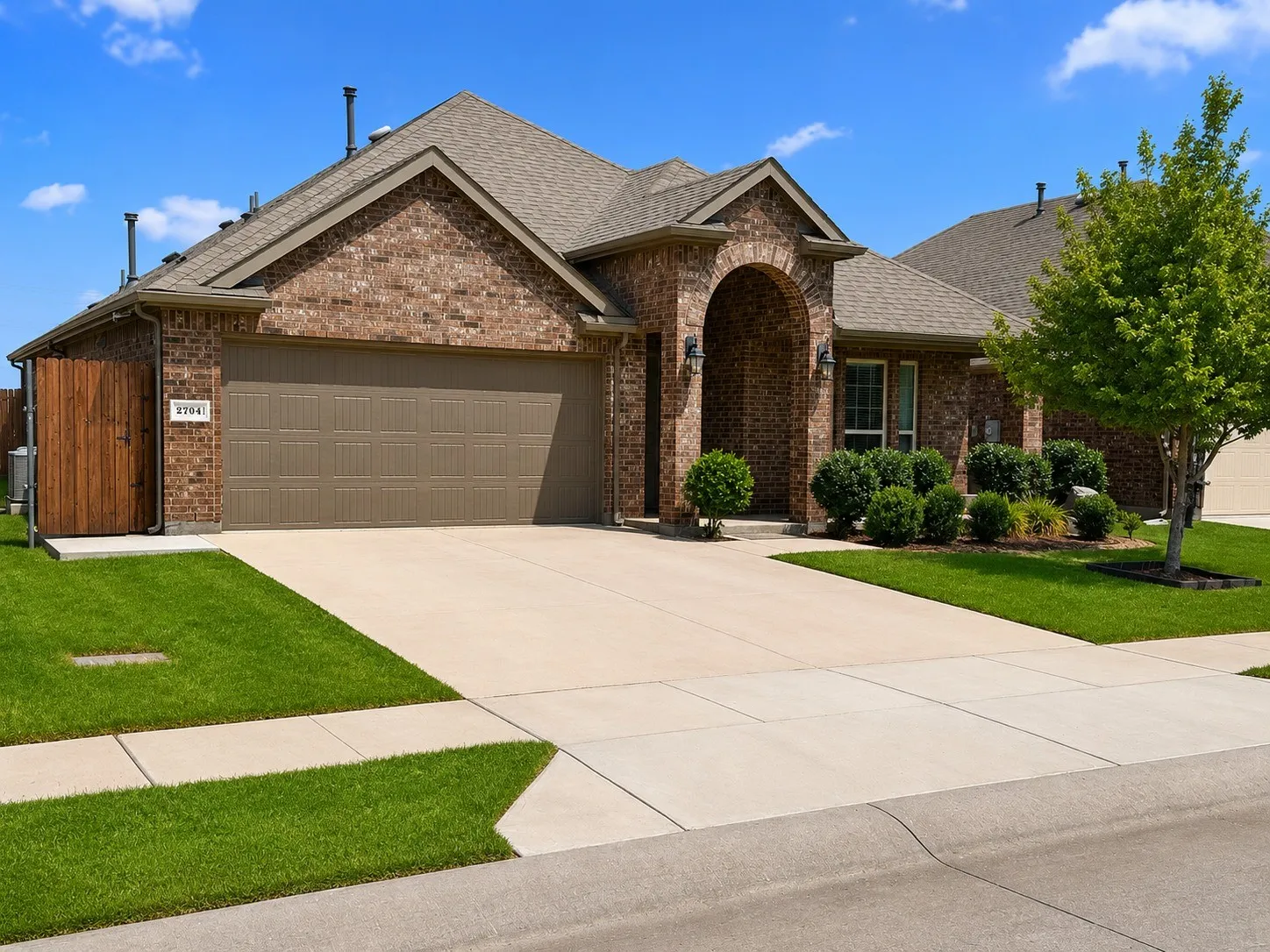 Brick exterior featuring an arched entryway, an attached two-car garage, manicured landscaping, and a concrete driveway