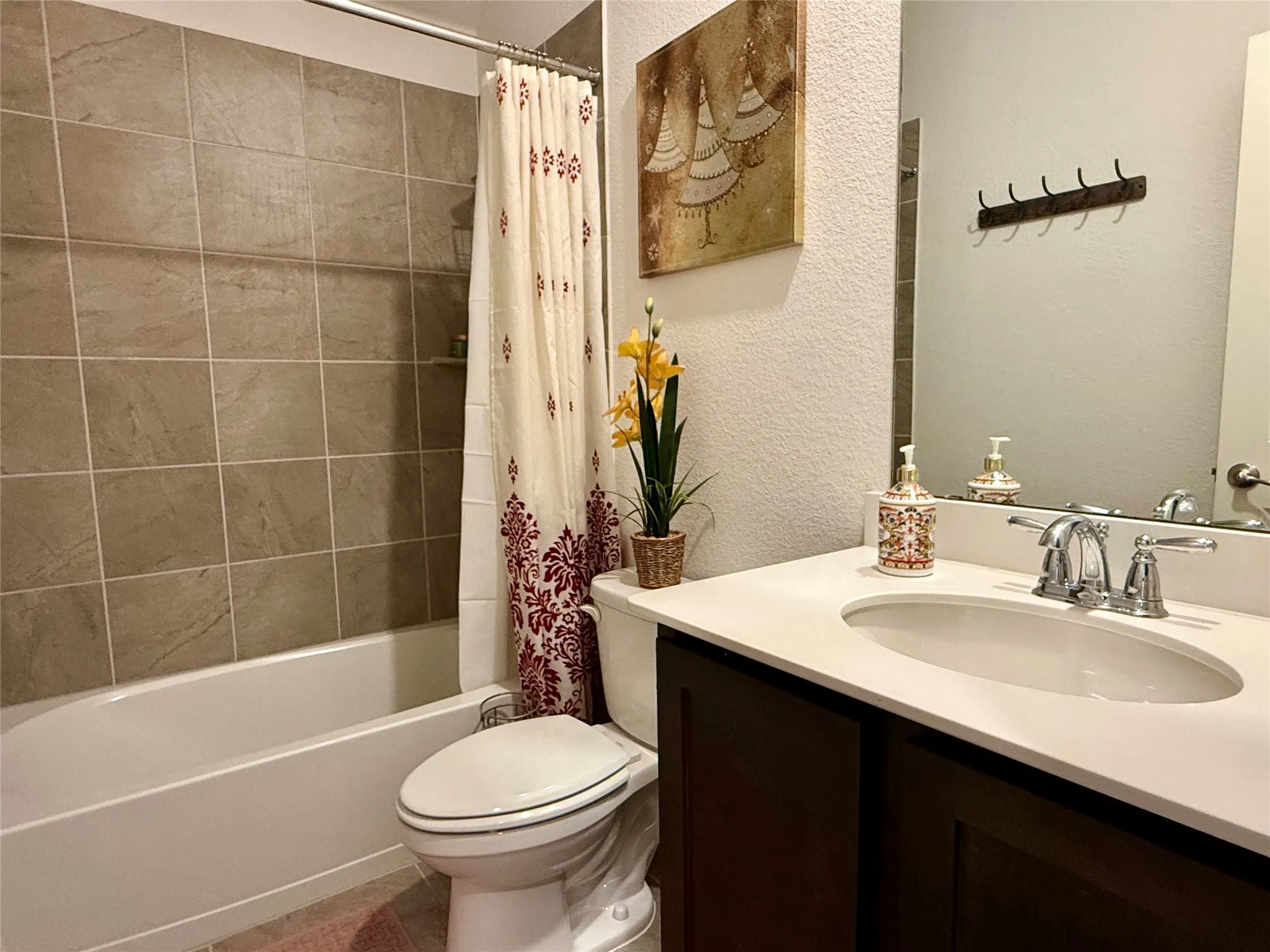 Bathroom featuring a dark wood-finish vanity with a white countertop and undermount sink, a chrome two-handle faucet, a toilet, and a bathtub with large format tile surround