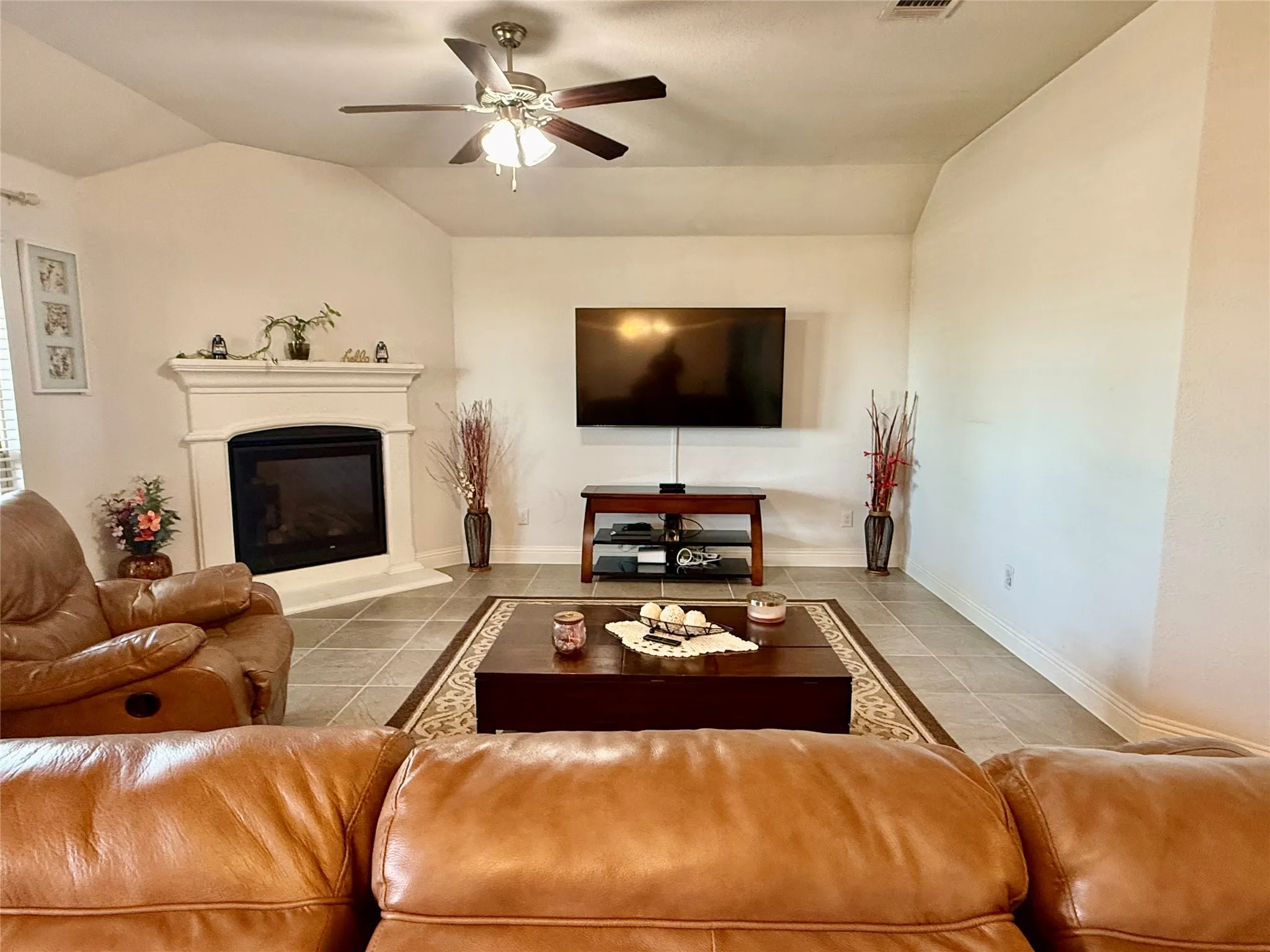 Living area featuring vaulted ceilings, a corner fireplace with a white mantel, and tile flooring