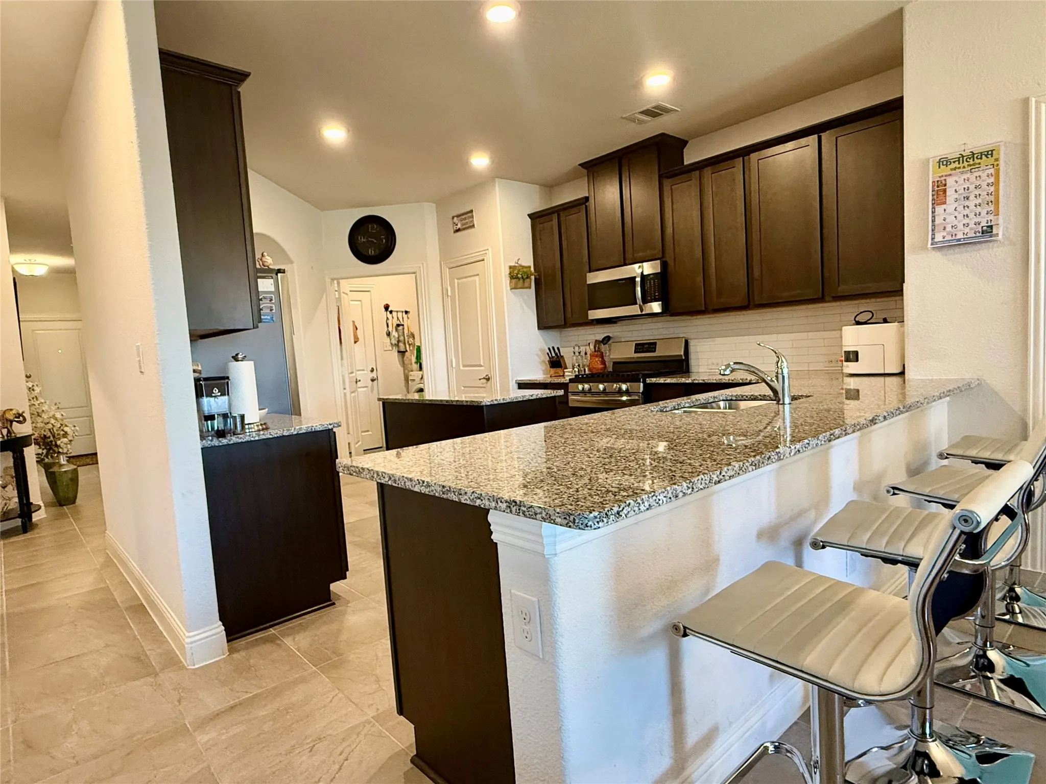 Kitchen featuring a U-shaped granite countertop, dark wood-finish cabinetry, stainless steel appliances, and a tiled backsplash