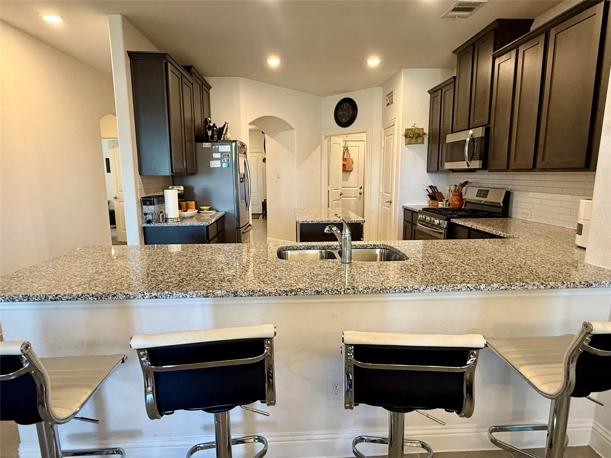 Kitchen featuring speckled granite countertops, dark wood cabinetry, a stainless steel sink with a gooseneck faucet, a white subway tile backsplash, and recessed lighting