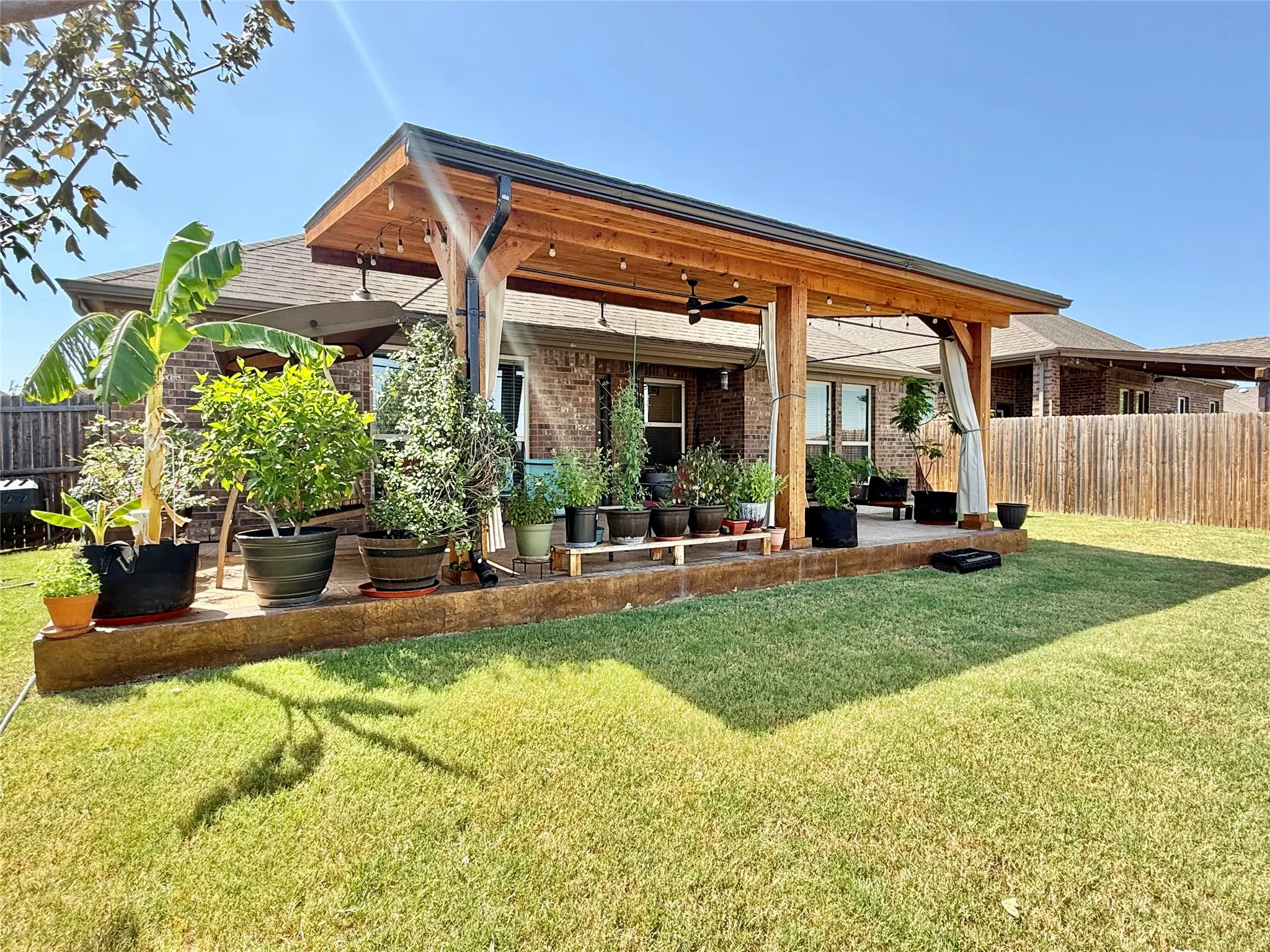Expansive backyard featuring a covered patio with a wood-finish ceiling, exposed beams, string lighting, and a ceiling fan