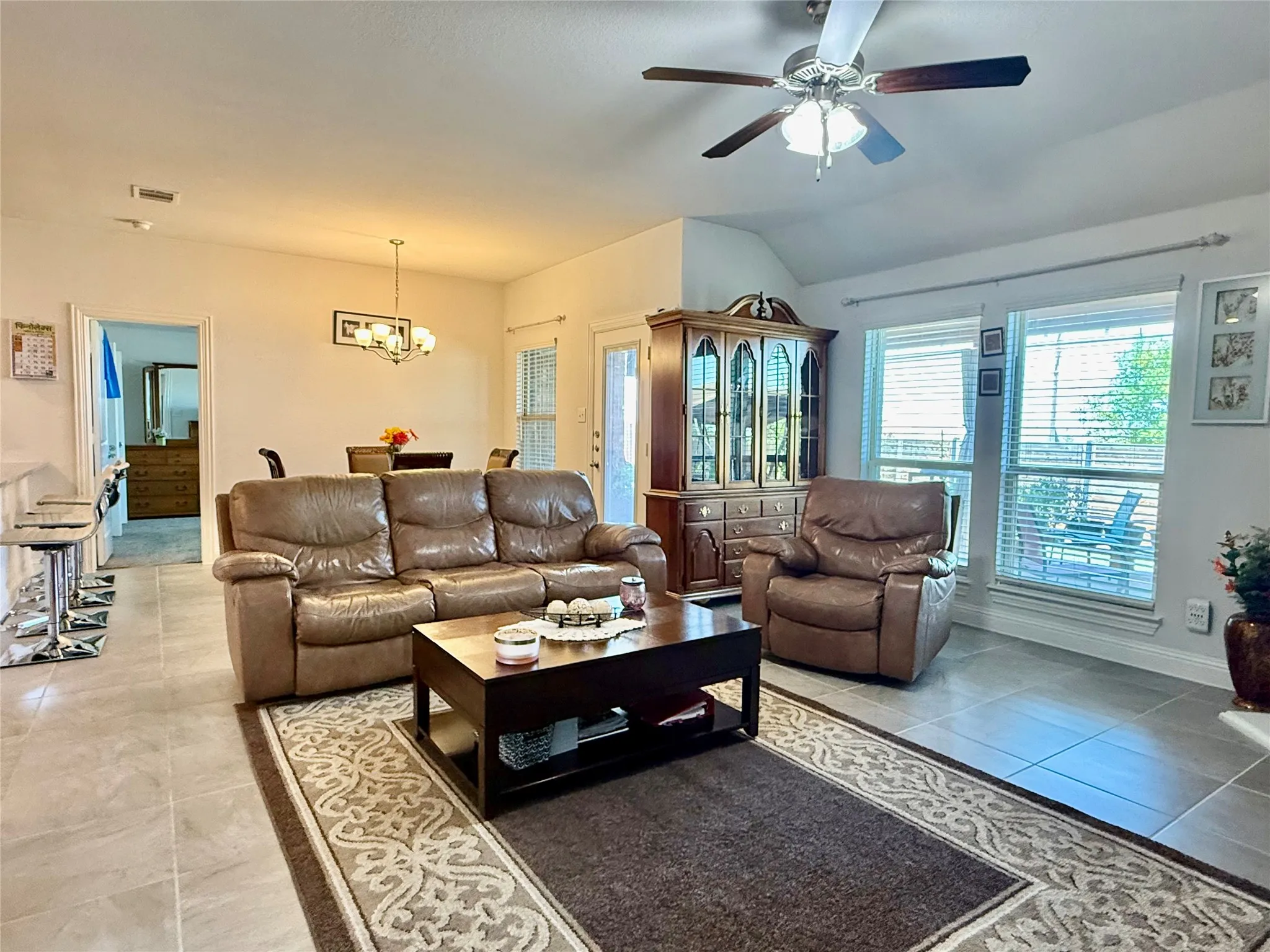 Expansive living area featuring tile flooring, a vaulted ceiling, and a ceiling fan with light fixture