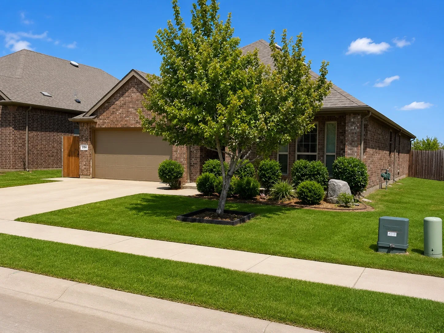 Brick exterior featuring a two-car garage, mature landscaping, and a fenced side yard