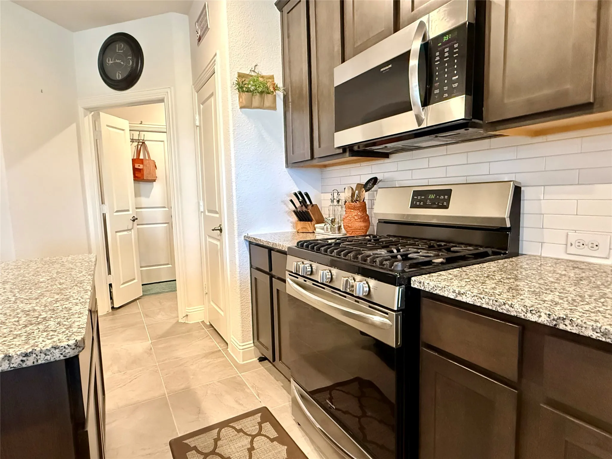 Kitchen featuring granite countertops, stainless steel gas range, coordinating microwave, dark wood cabinetry, and a subway tile backsplash