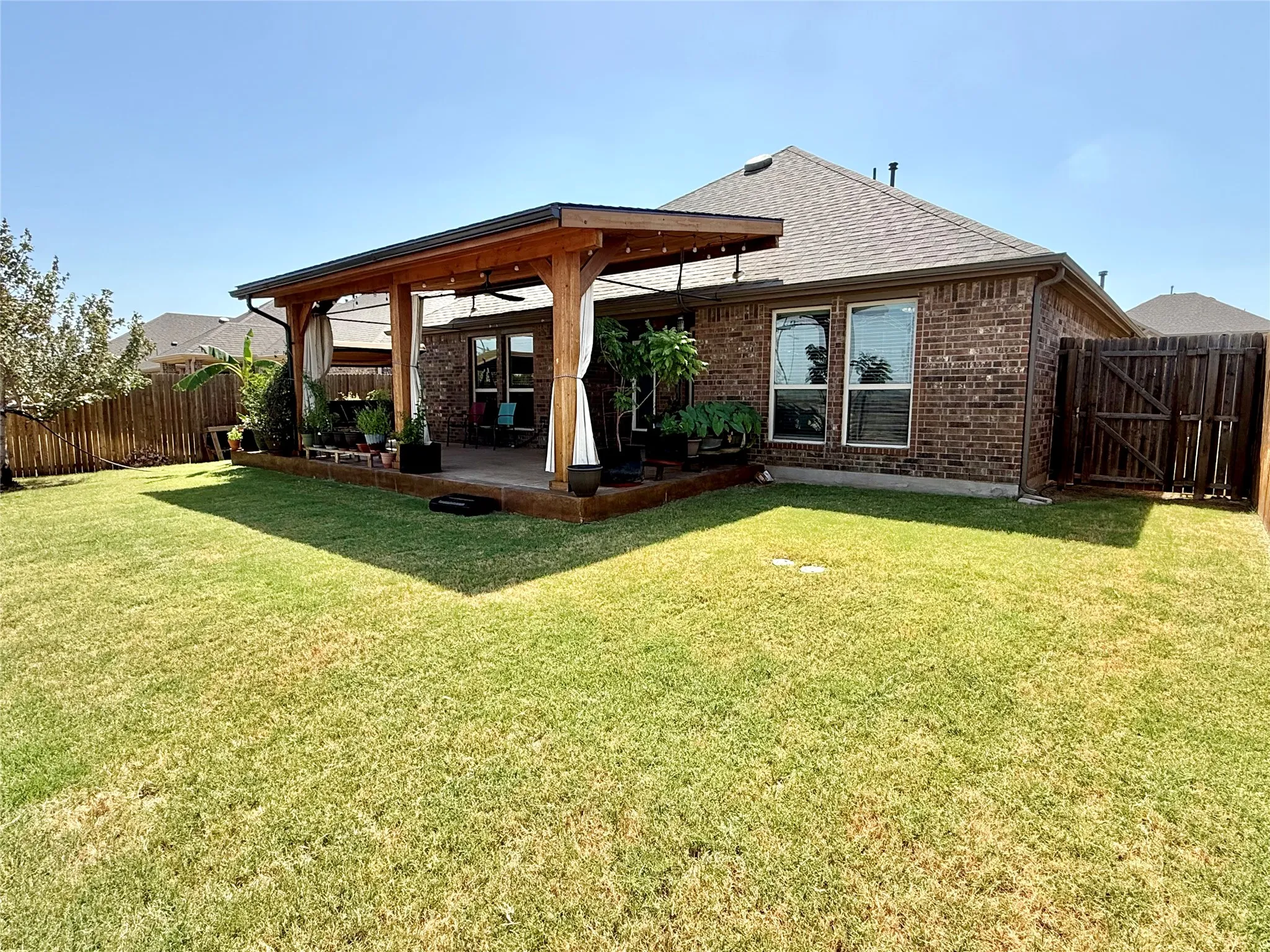 Expansive backyard featuring a covered patio with a wood-beam pergola, string lighting, and ceiling fan