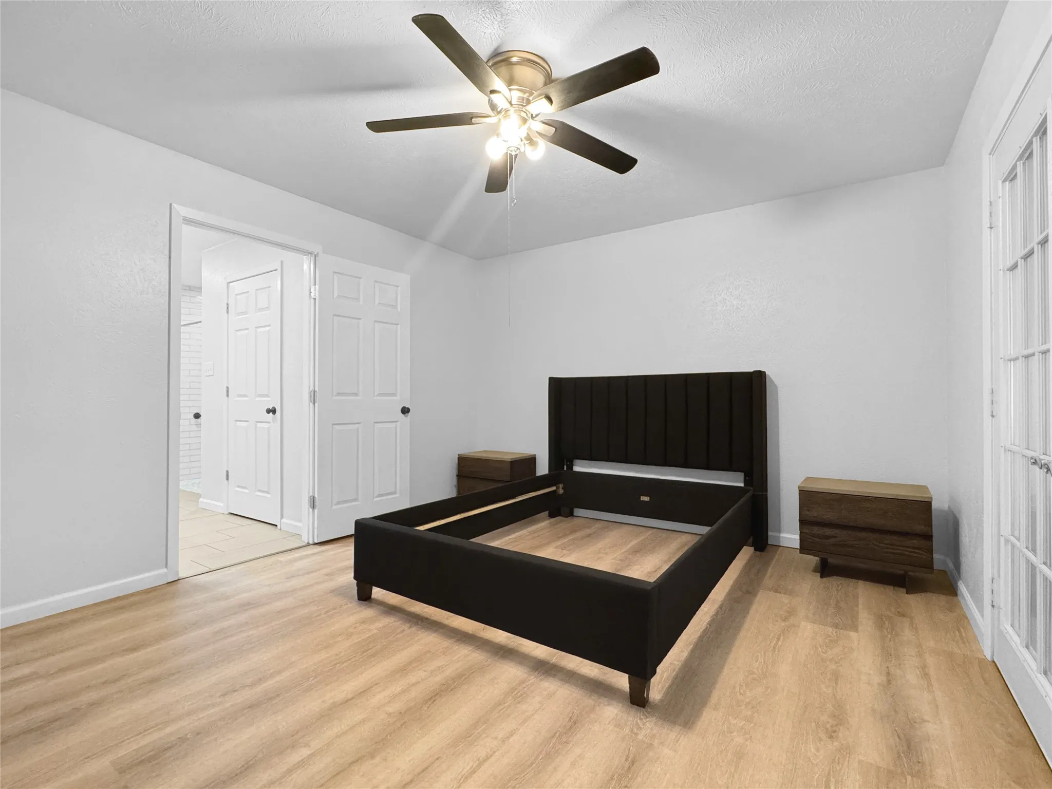 Light wood-finish flooring with a ceiling fan featuring a brushed nickel base and dark blades