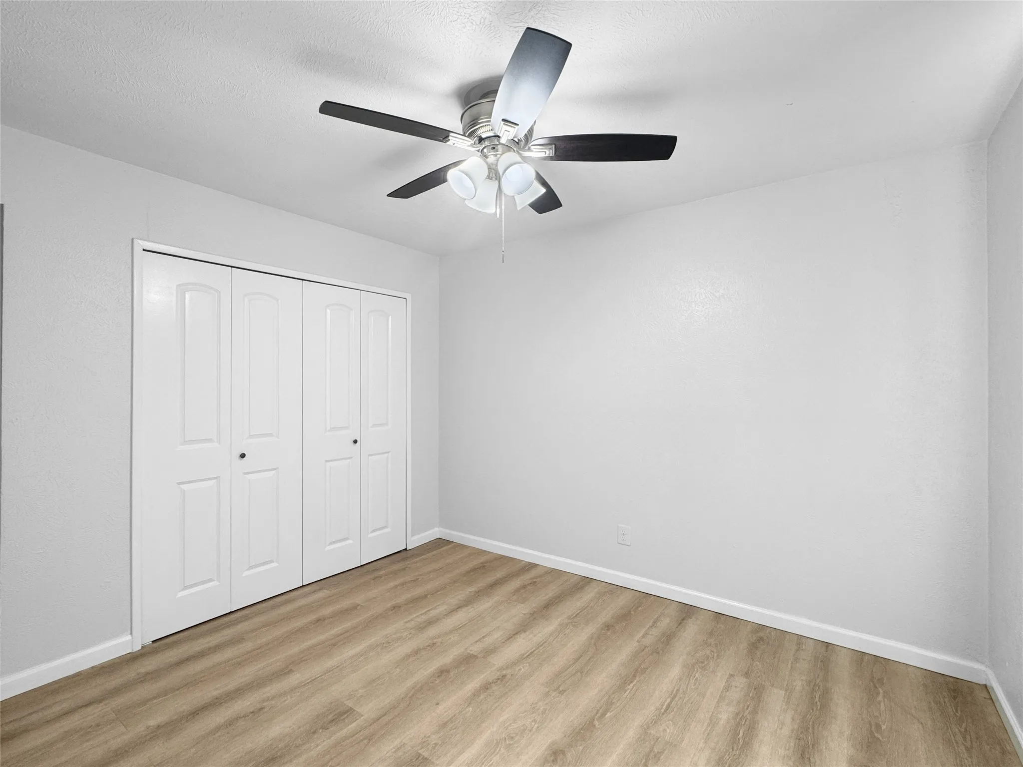 Room featuring wood-finish flooring, white walls, and a ceiling fan with integrated lighting
