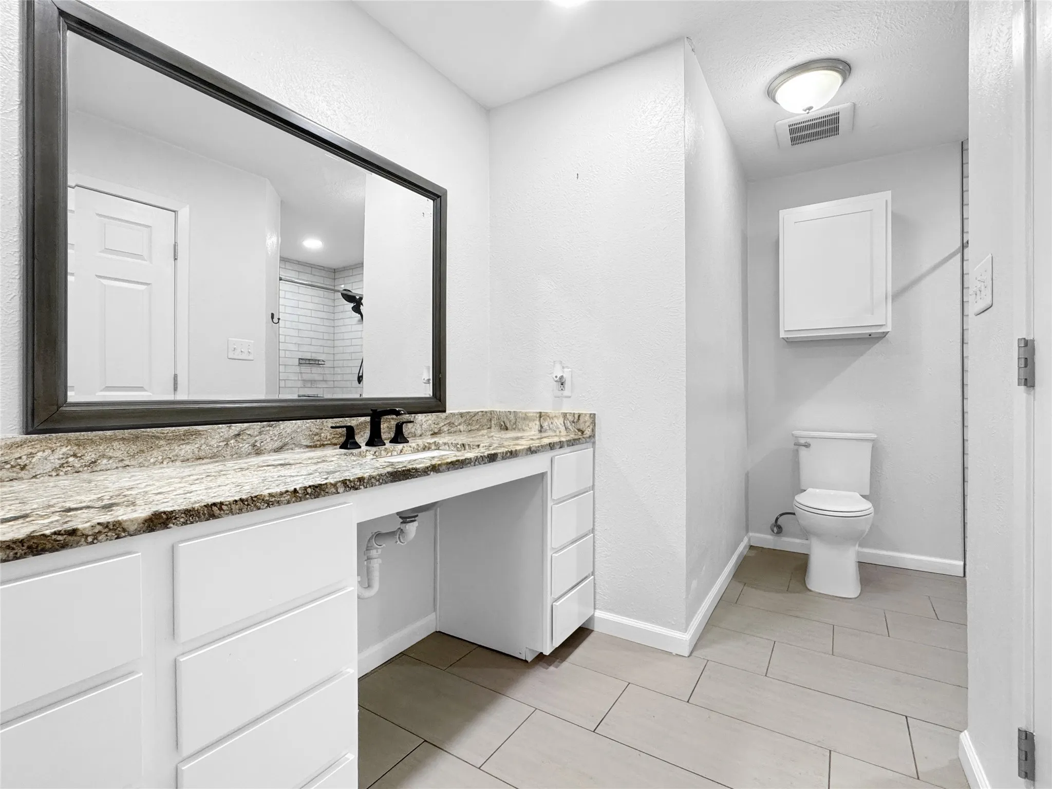 Spacious bathroom featuring a single vanity with a granite-style countertop, white cabinetry with matte black hardware, and a large framed mirror