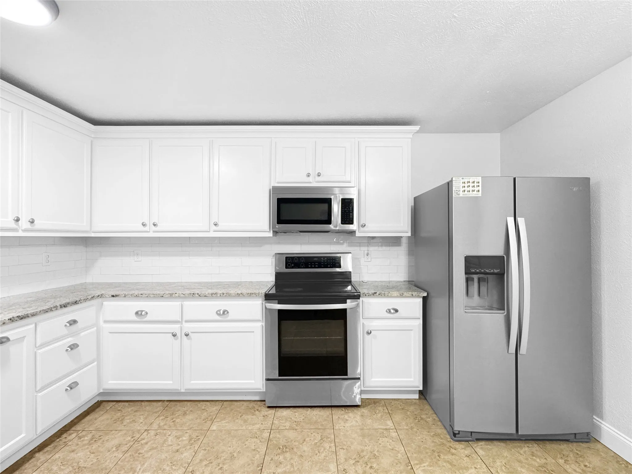 Modern kitchen featuring white cabinetry, granite-style countertops, and a white subway tile backsplash