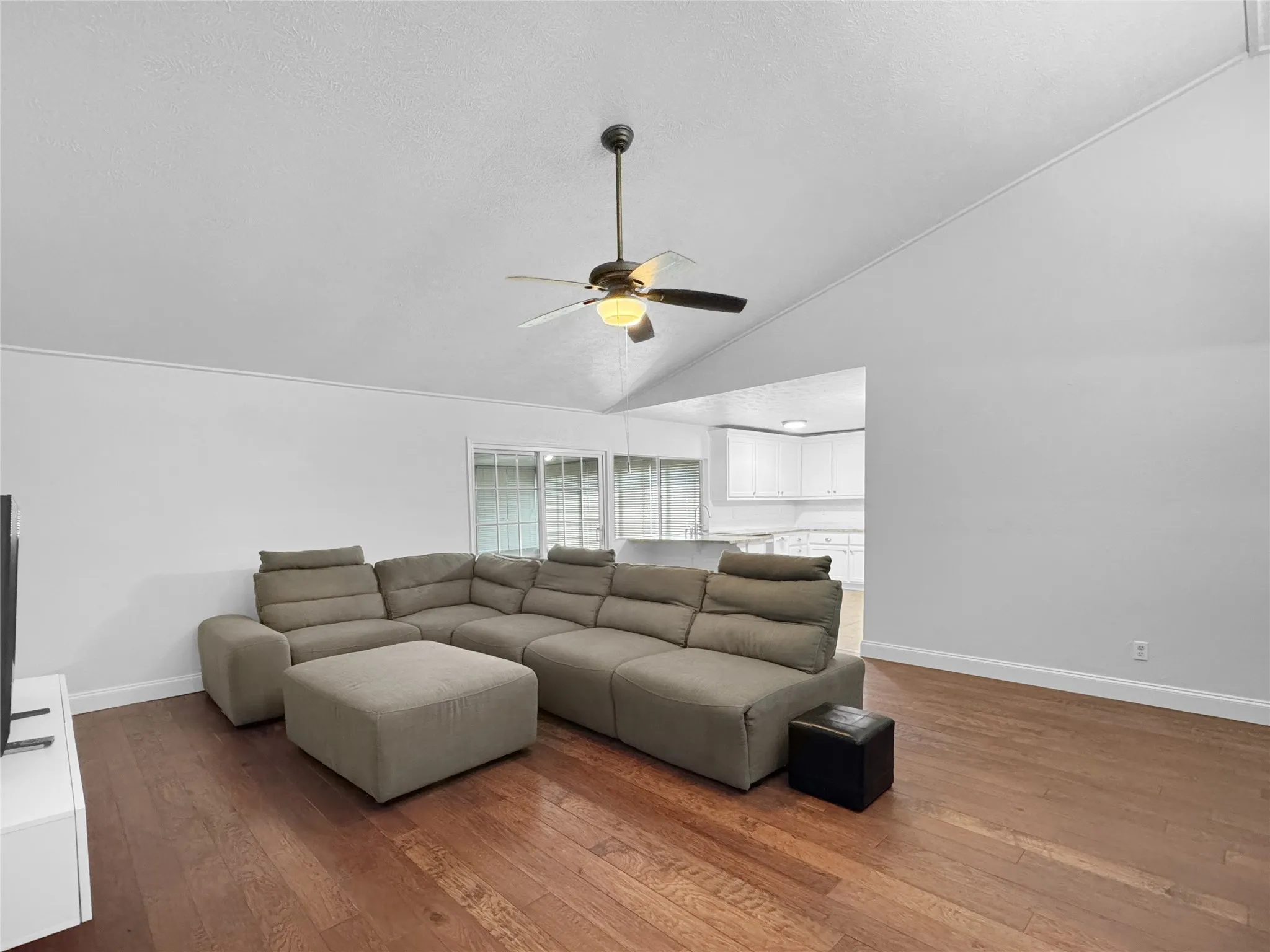Living area featuring hardwood flooring, vaulted ceiling, and a ceiling fan with integrated lighting