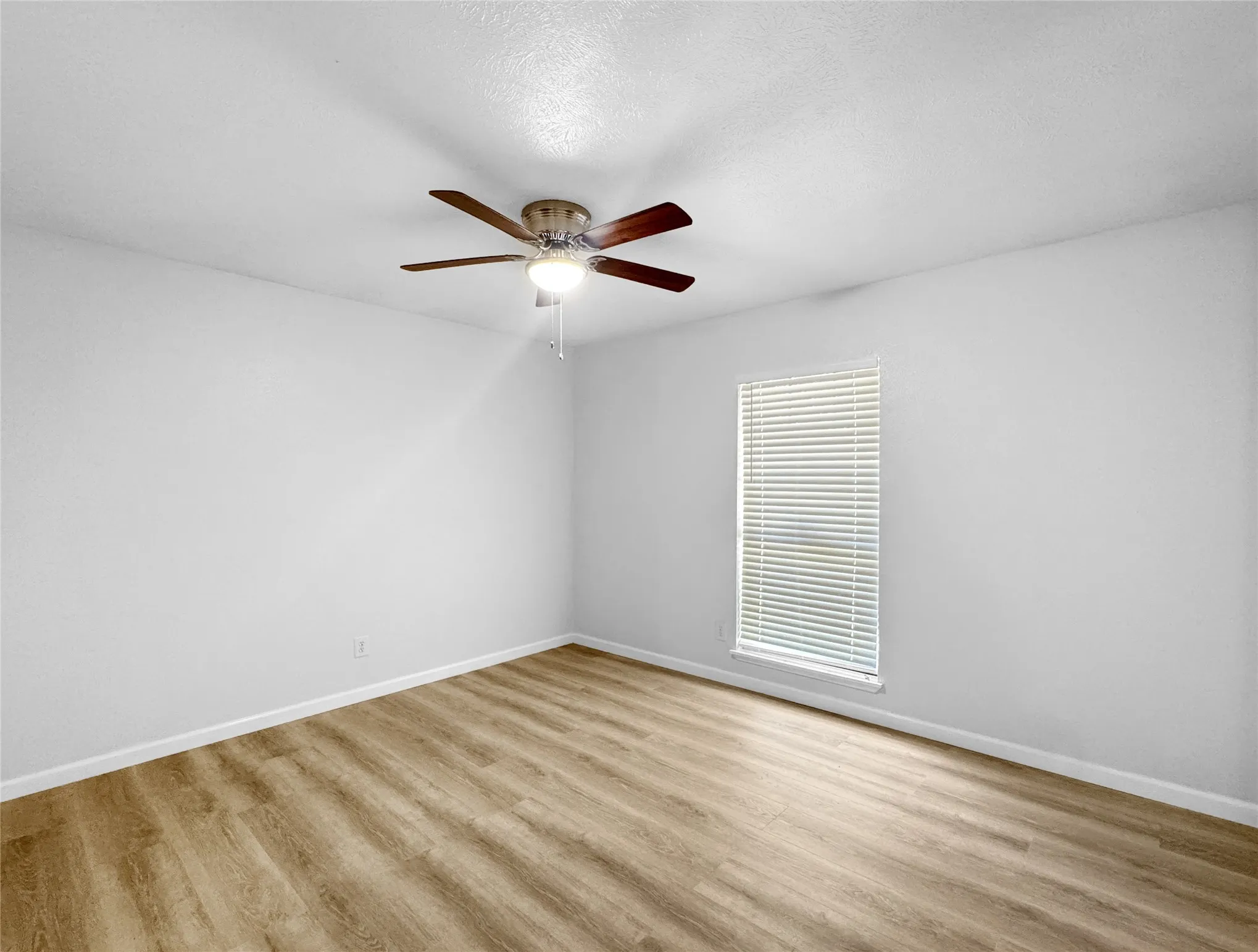 Room featuring wood-finish flooring, white walls, and a window with horizontal blinds