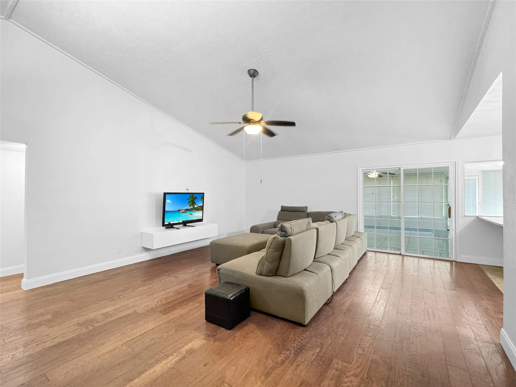 Living area featuring wood-finish flooring, a vaulted ceiling with a ceiling fan, and white baseboards