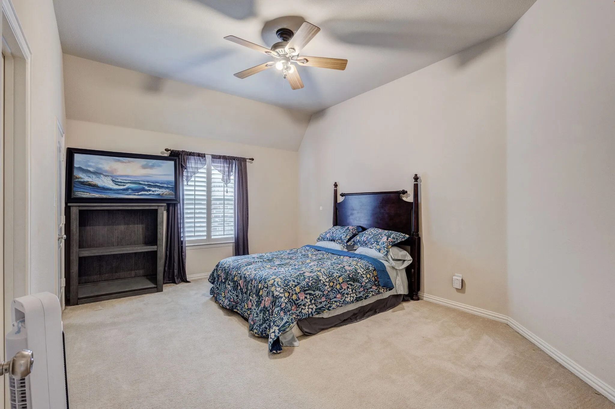 Carpeted room featuring a window with plantation shutters and drapes, a ceiling fan with light fixture, and a built-in shelving unit