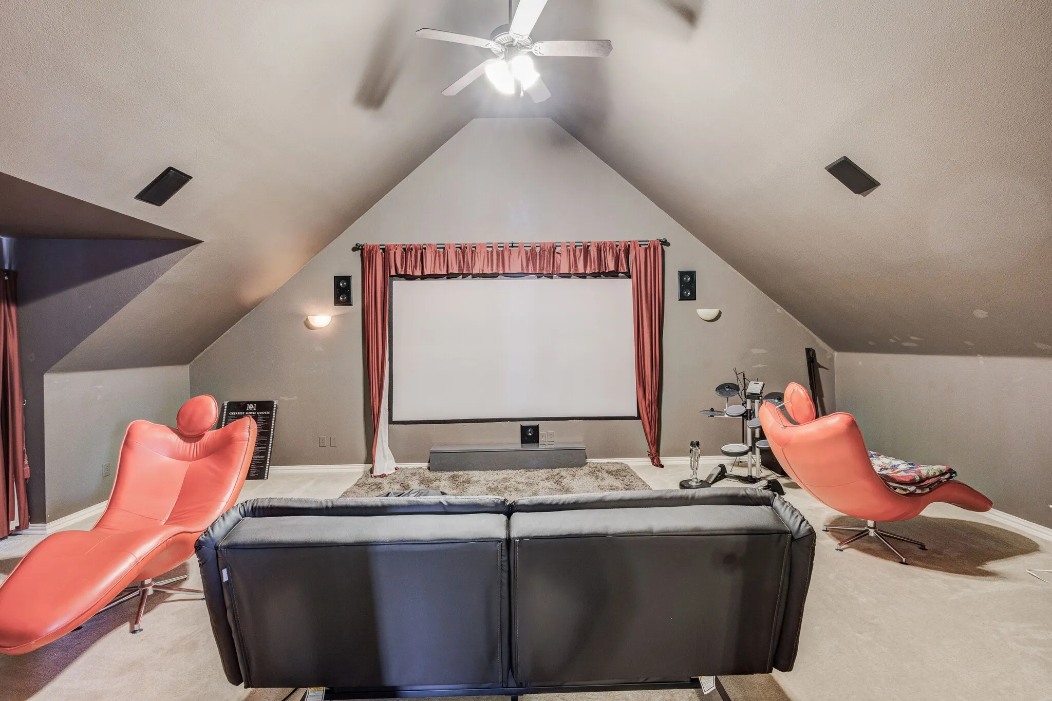 Carpeted media room featuring an angled ceiling, ceiling fan with integrated lighting, and a wall-mounted projection screen