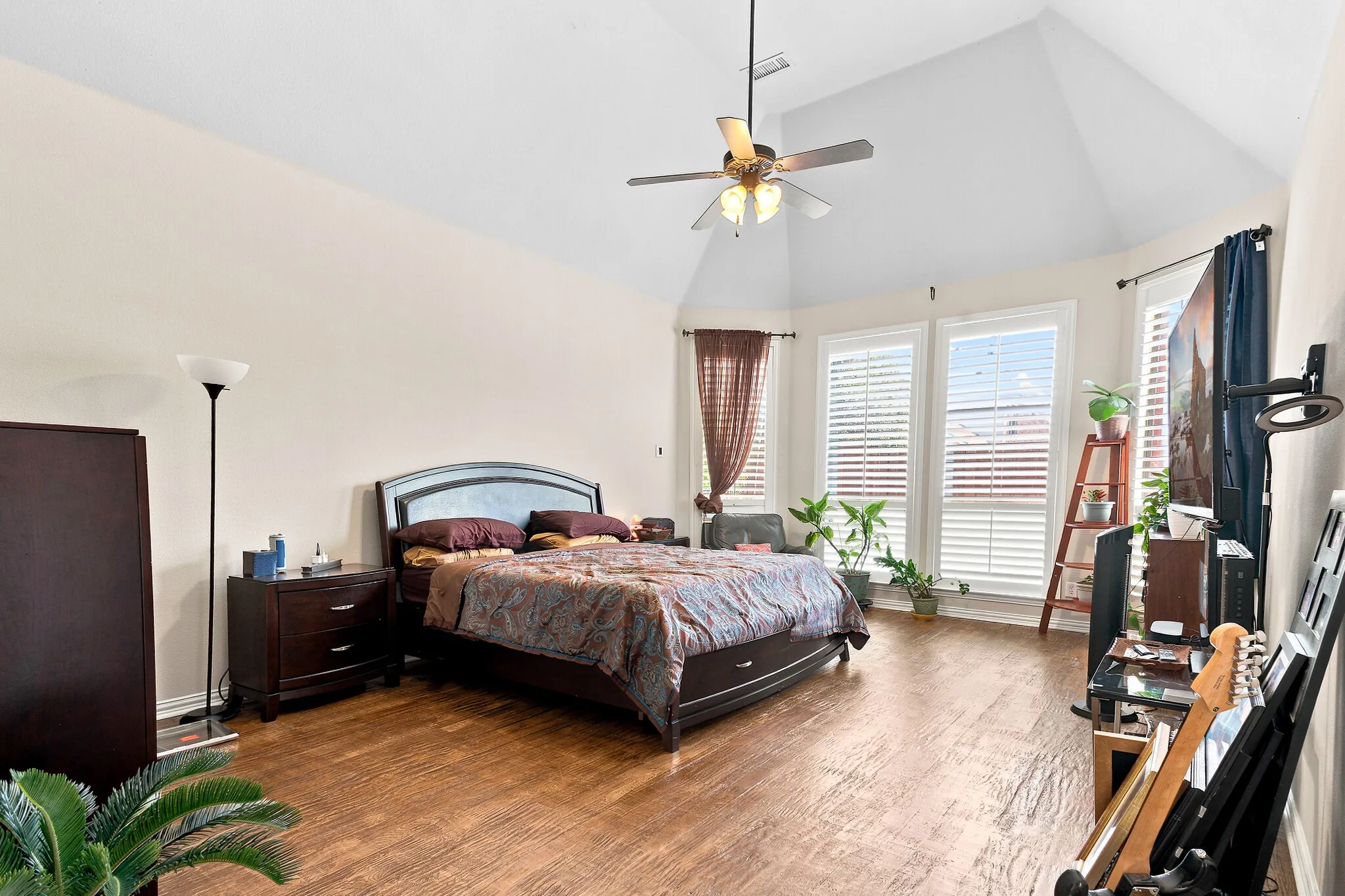 Spacious room featuring wood-finish flooring, vaulted ceiling with a ceiling fan, and multiple windows with horizontal blinds