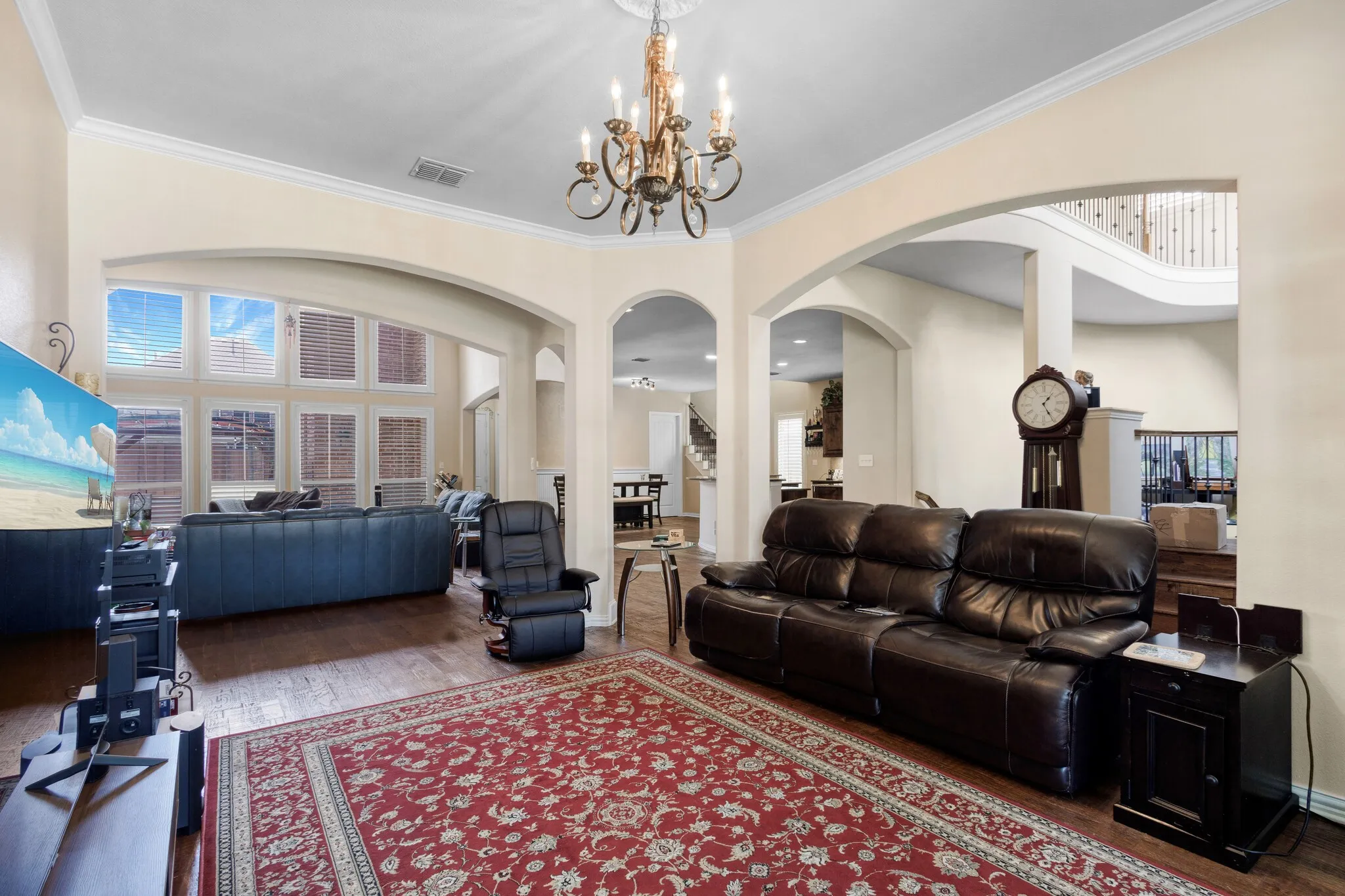 Spacious room featuring wood-finish flooring, high ceilings with crown molding, and a chandelier