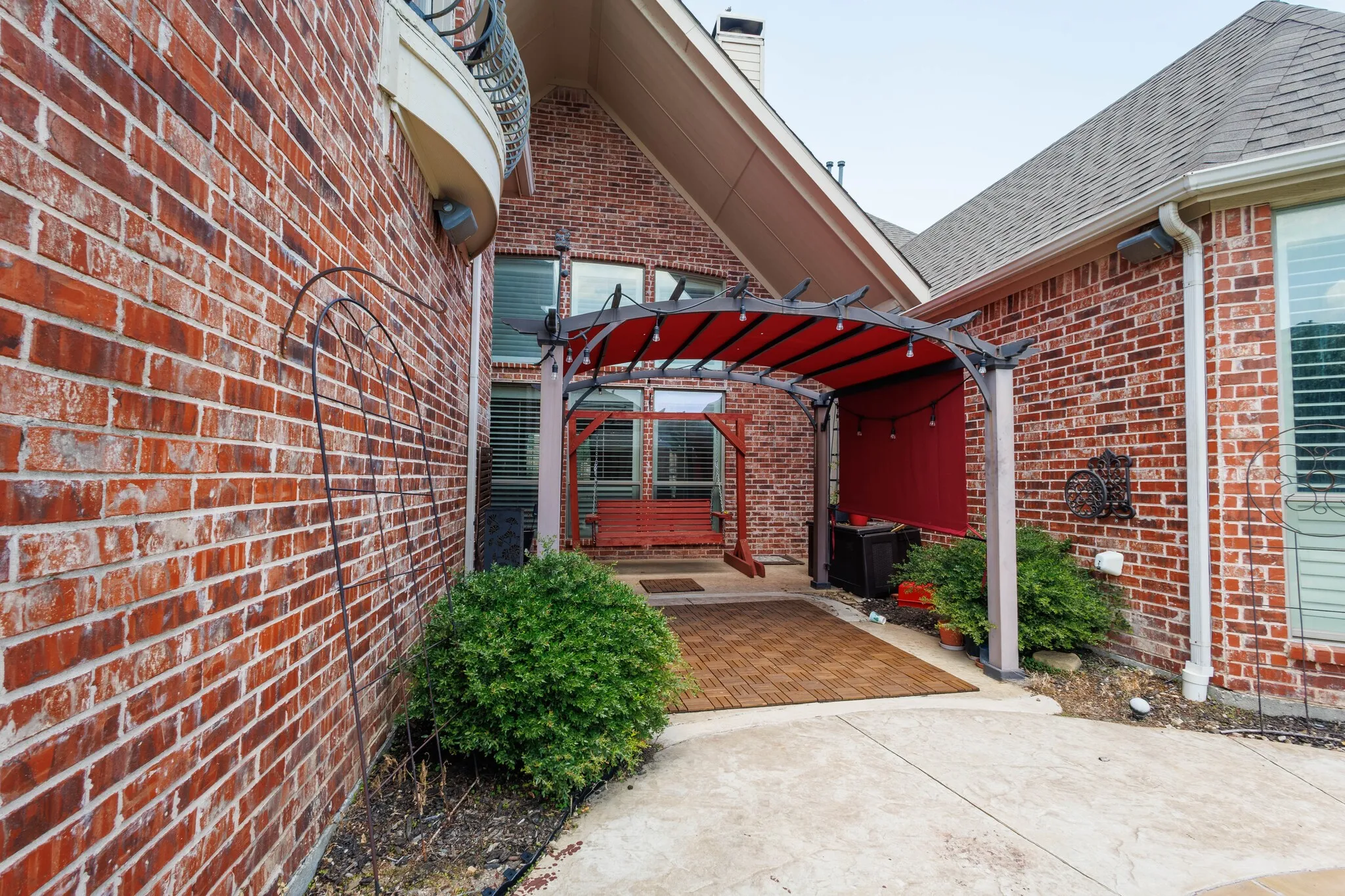 Brick exterior with a gabled roofline and an outdoor pergola featuring a red fabric canopy