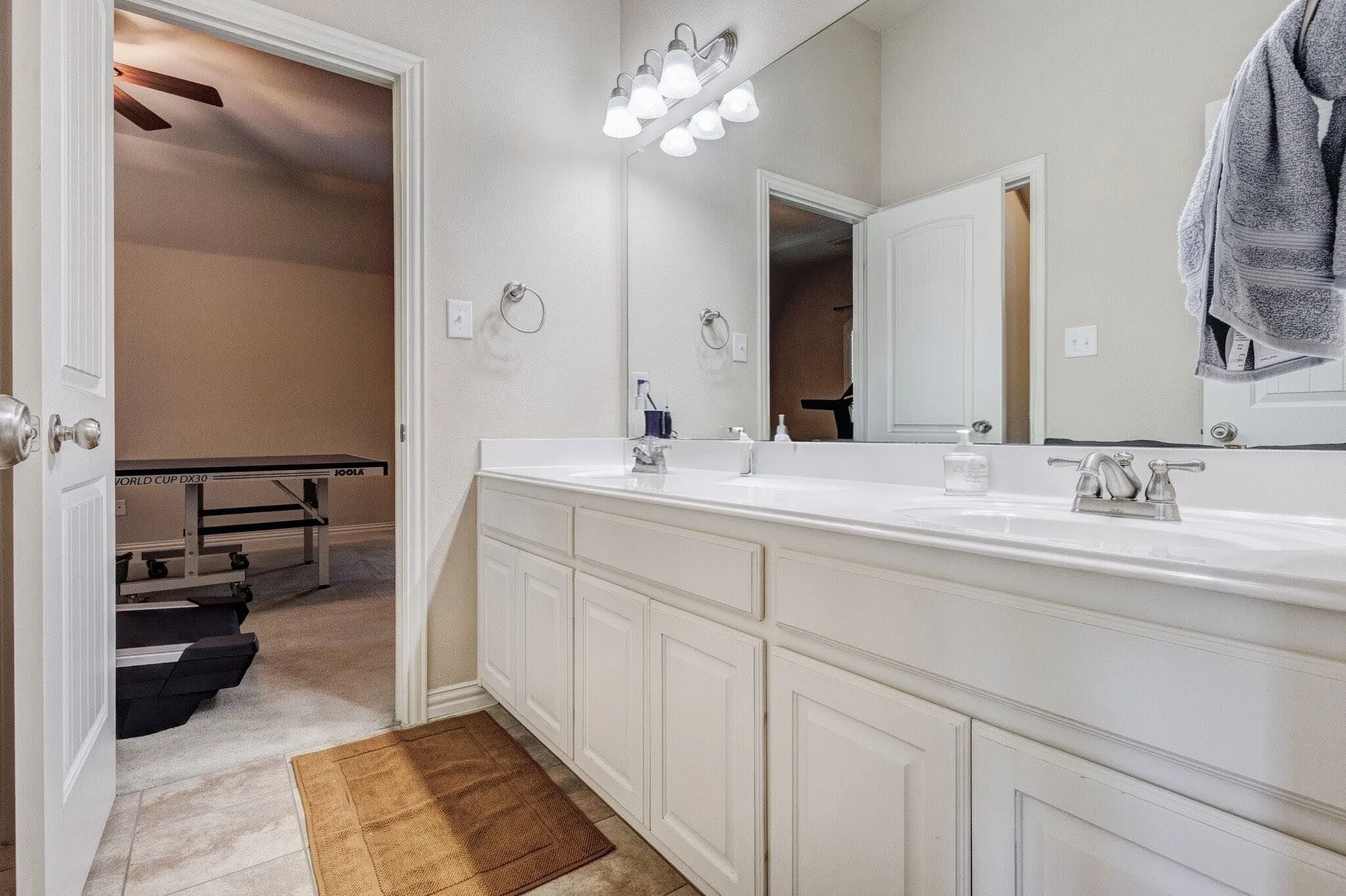 Double vanity with white cabinetry, integrated sinks, chrome fixtures, and a large wall-mounted mirror