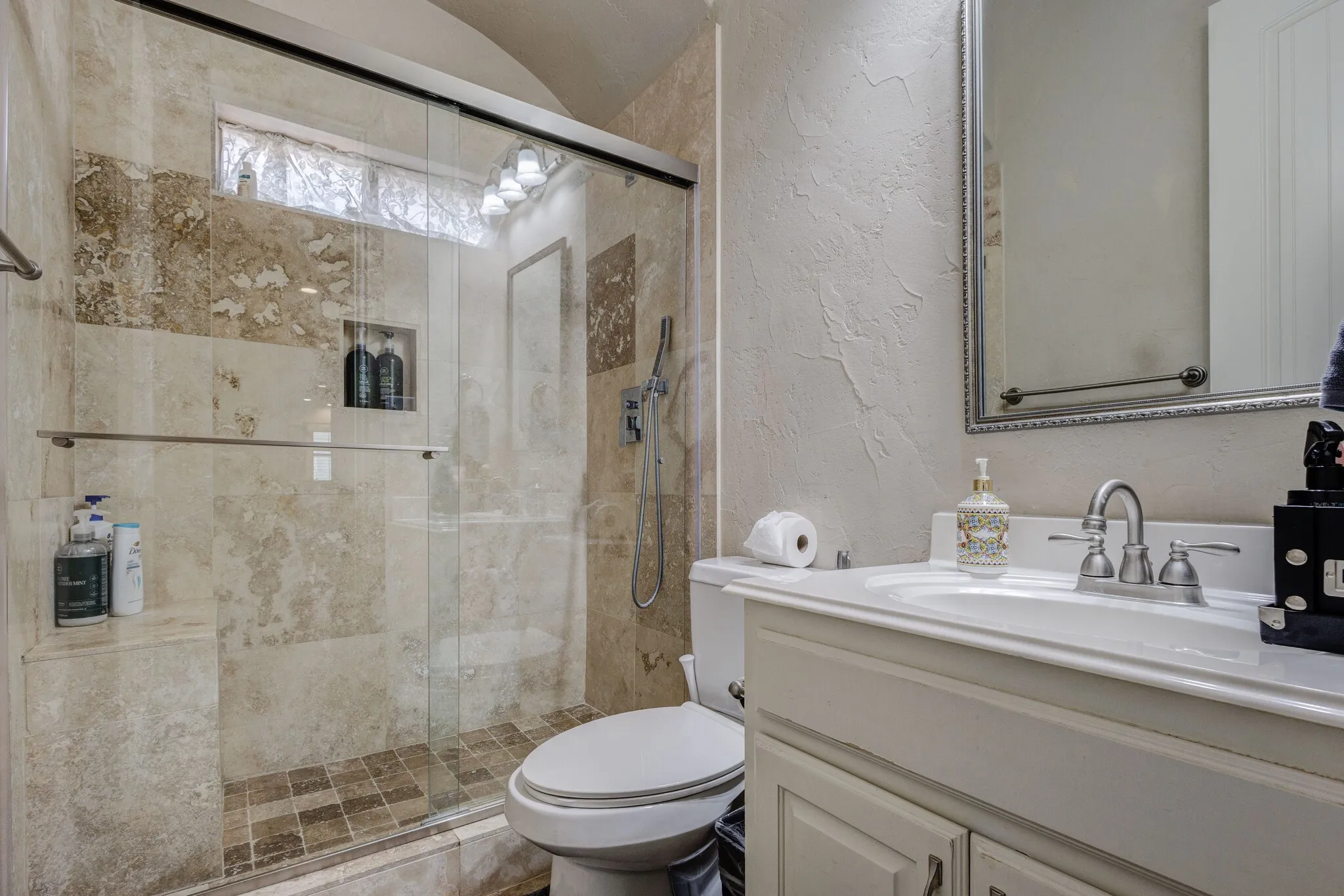 Bathroom featuring a glass-enclosed shower with full-height tile surround, an integrated shower niche, and a separate shower bench