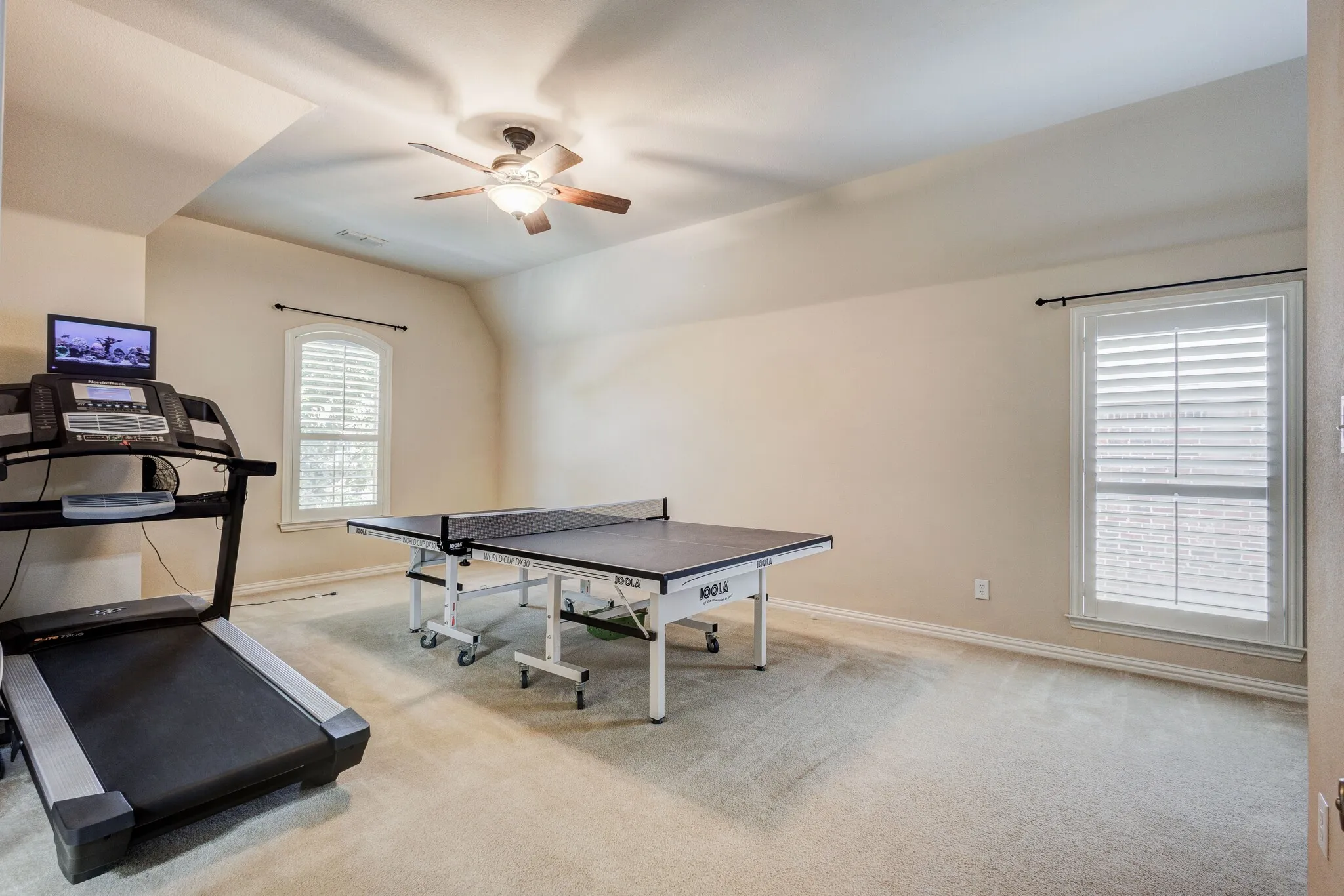 Carpeted room with a ceiling fan, two windows with white plantation shutters, and sloped ceiling details