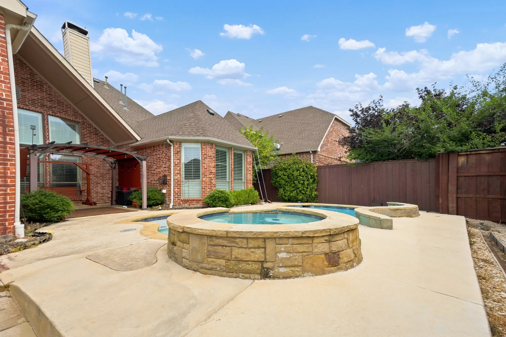 Brick exterior with a multi-level roofline, featuring a stone-clad circular spa, an adjacent freeform pool, and a concrete patio