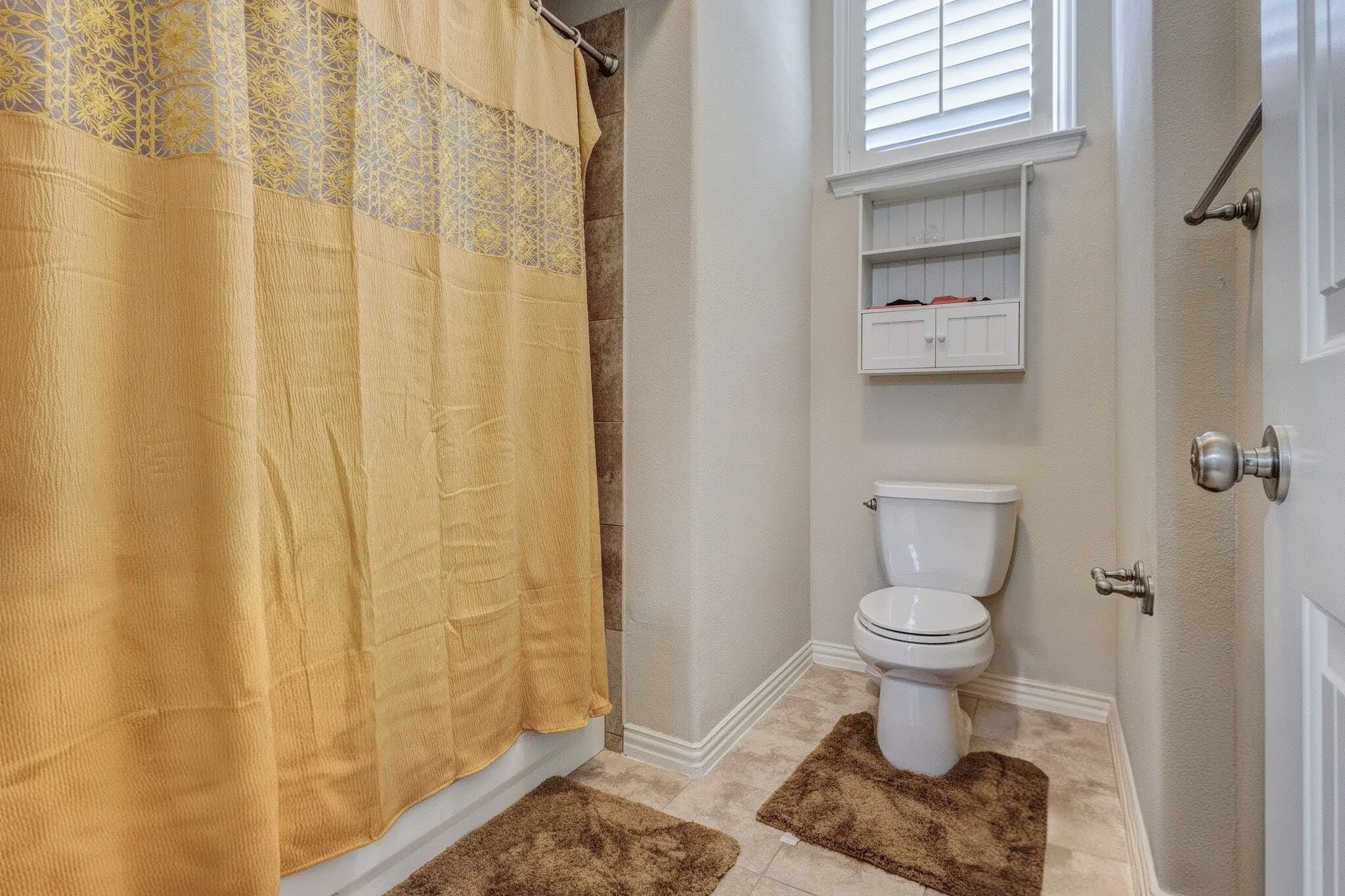 Bathroom with a white toilet, shuttered window, and a built-in wall cabinet featuring two lower doors