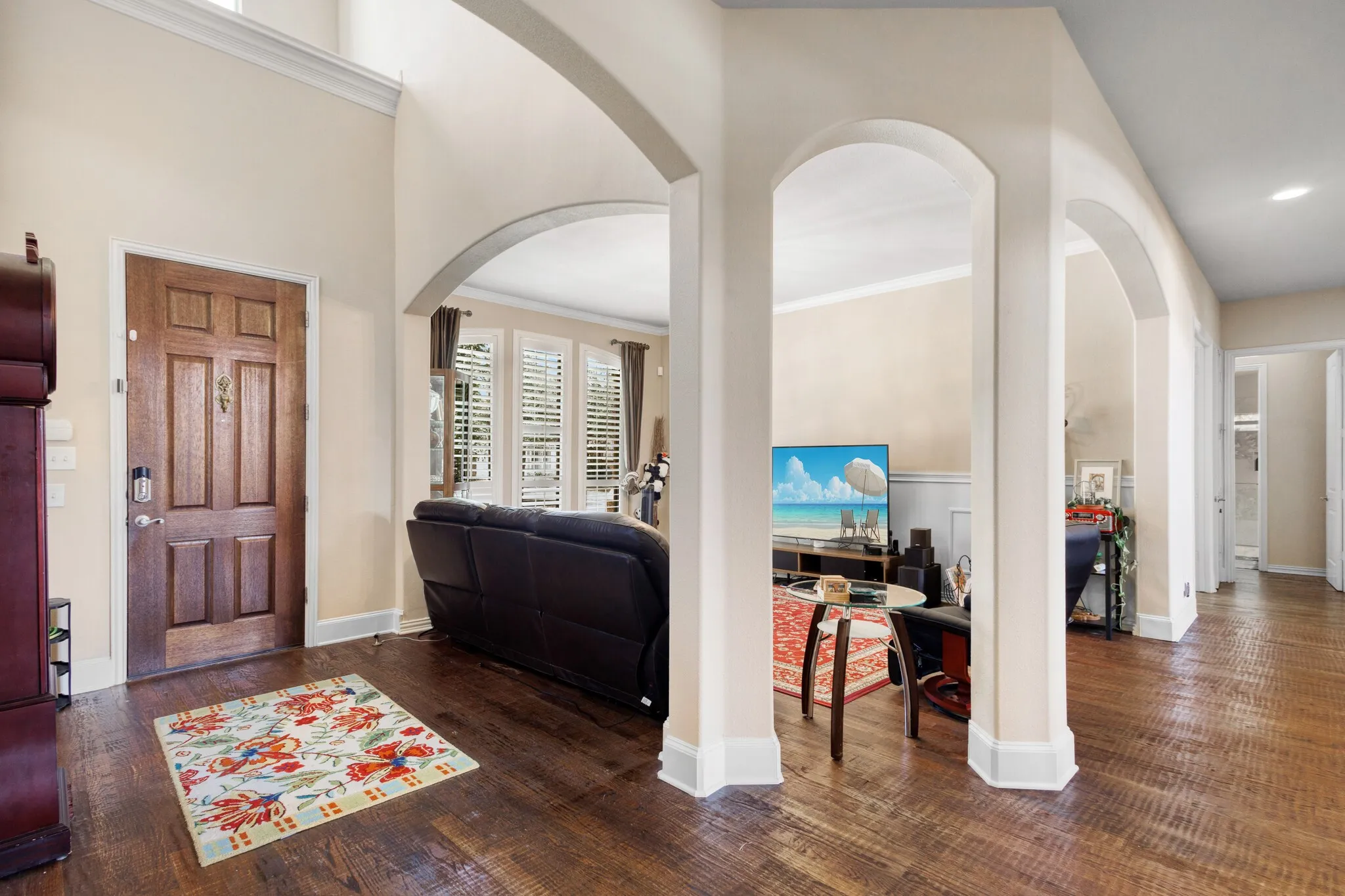 Foyer featuring a paneled wood entry door, high ceilings with crown molding, wood-finish flooring, and arched doorways opening to interior spaces