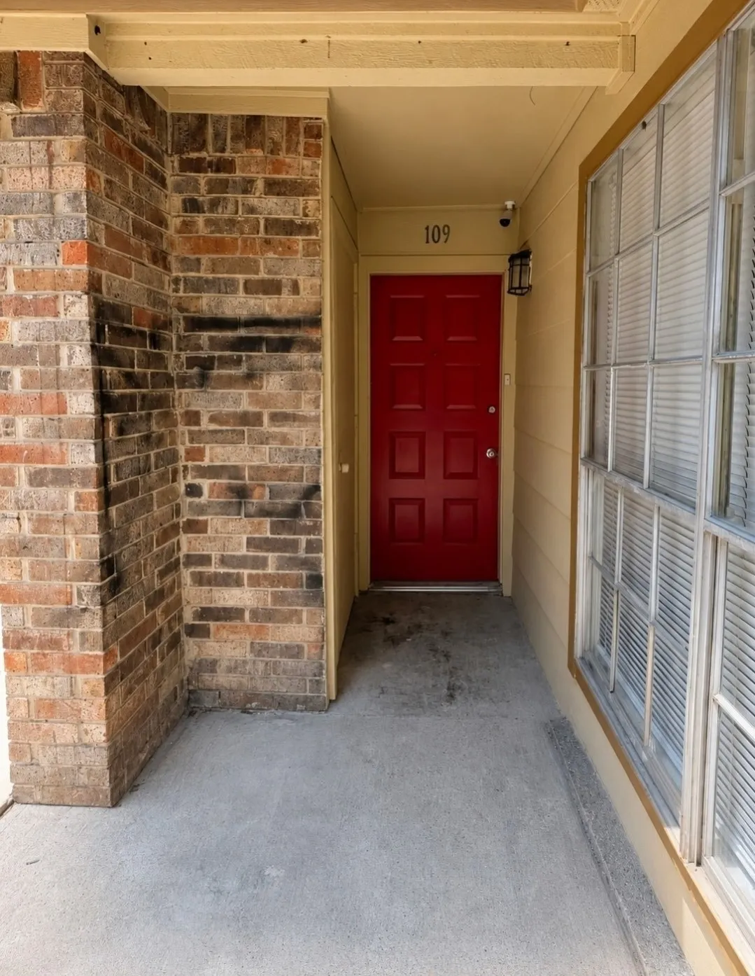 Vibrant red paneled door, brick exterior accents, and a fixed window with horizontal blinds