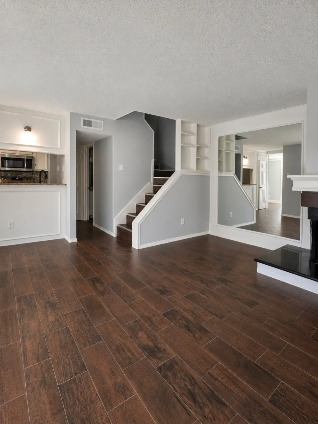 Open-concept living space with wood-finish flooring, built-in shelving, a fireplace with a black hearth, and a kitchen pass-through
