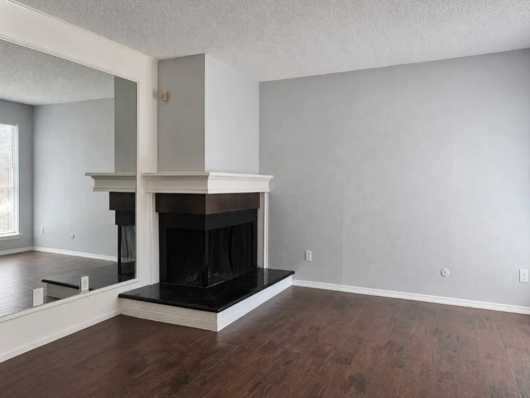 Living area featuring a corner fireplace with a black stone hearth and a white wood mantel, dark wood-finish flooring, and a large wall-mounted mirror