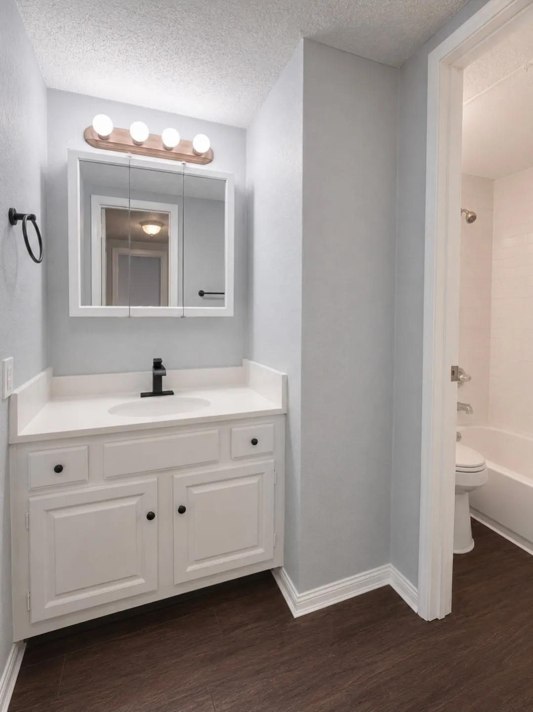 Bathroom featuring a white vanity with integrated sink, a black faucet, and a wood-finish flooring