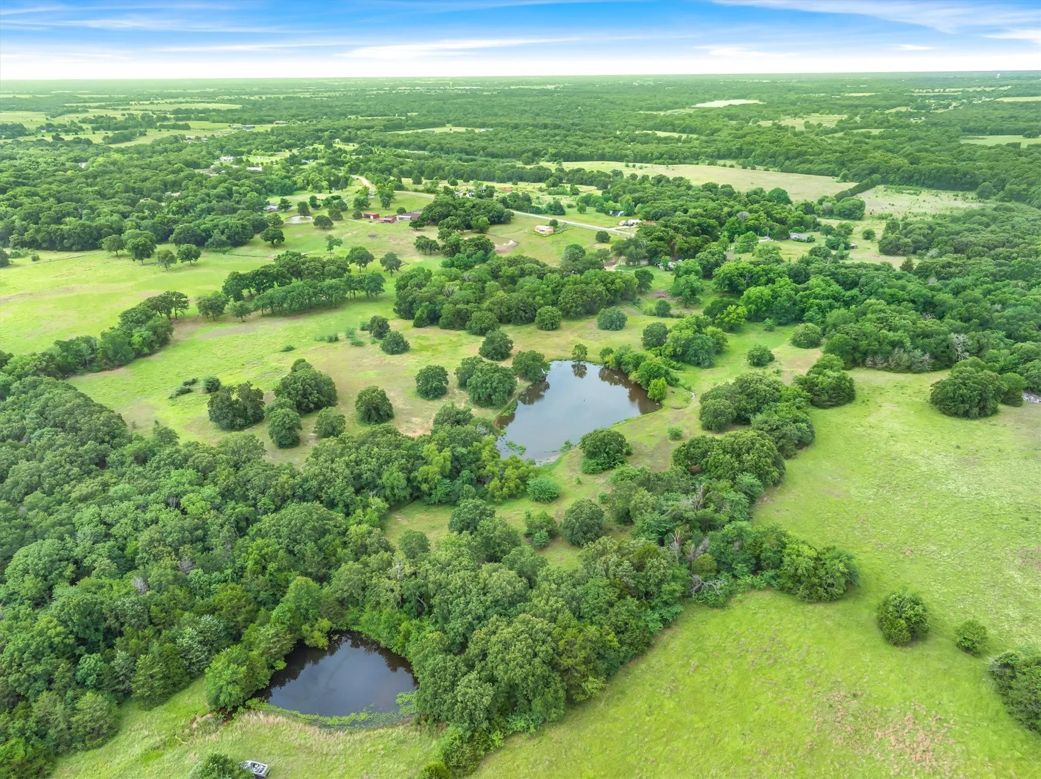 Expansive aerial landscape featuring multiple ponds, abundant mature trees, and vast green spaces