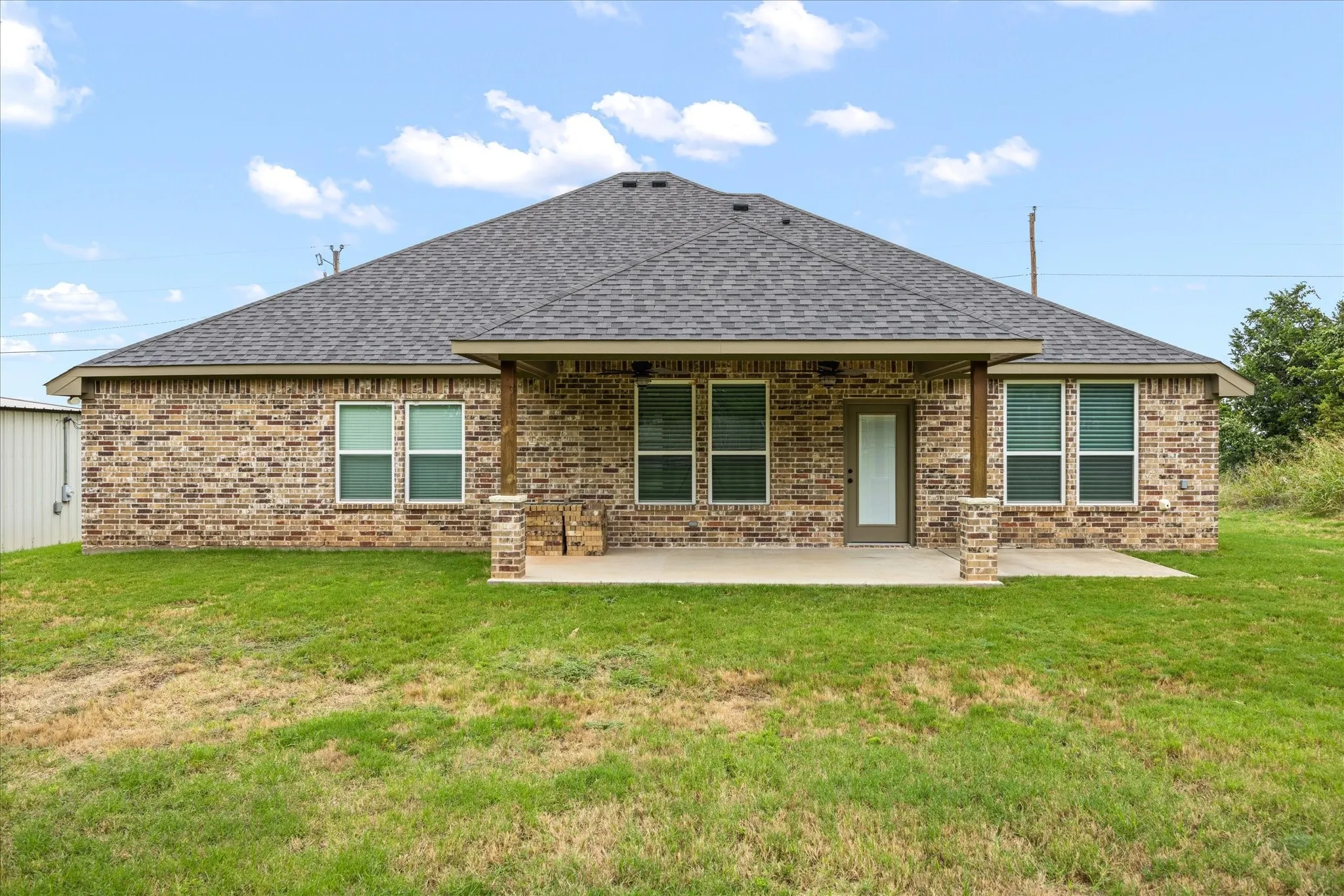 Rear brick exterior featuring a covered patio, multiple windows, and a dark shingle roof