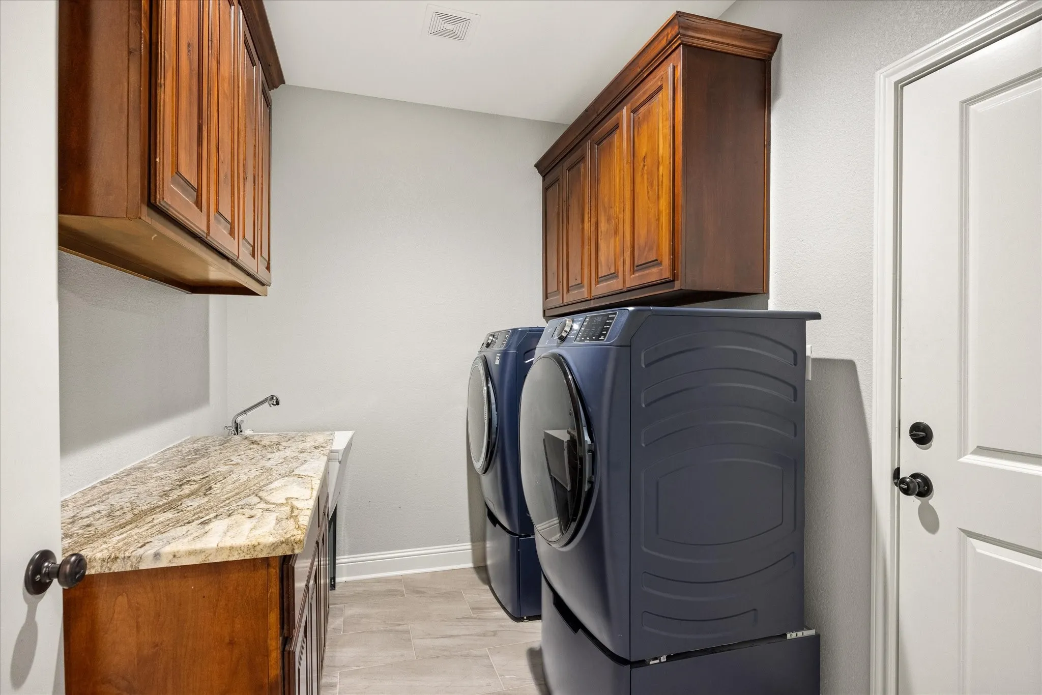 Laundry room featuring wood-finish cabinetry, a light-toned countertop with an integrated sink, and light gray tile flooring