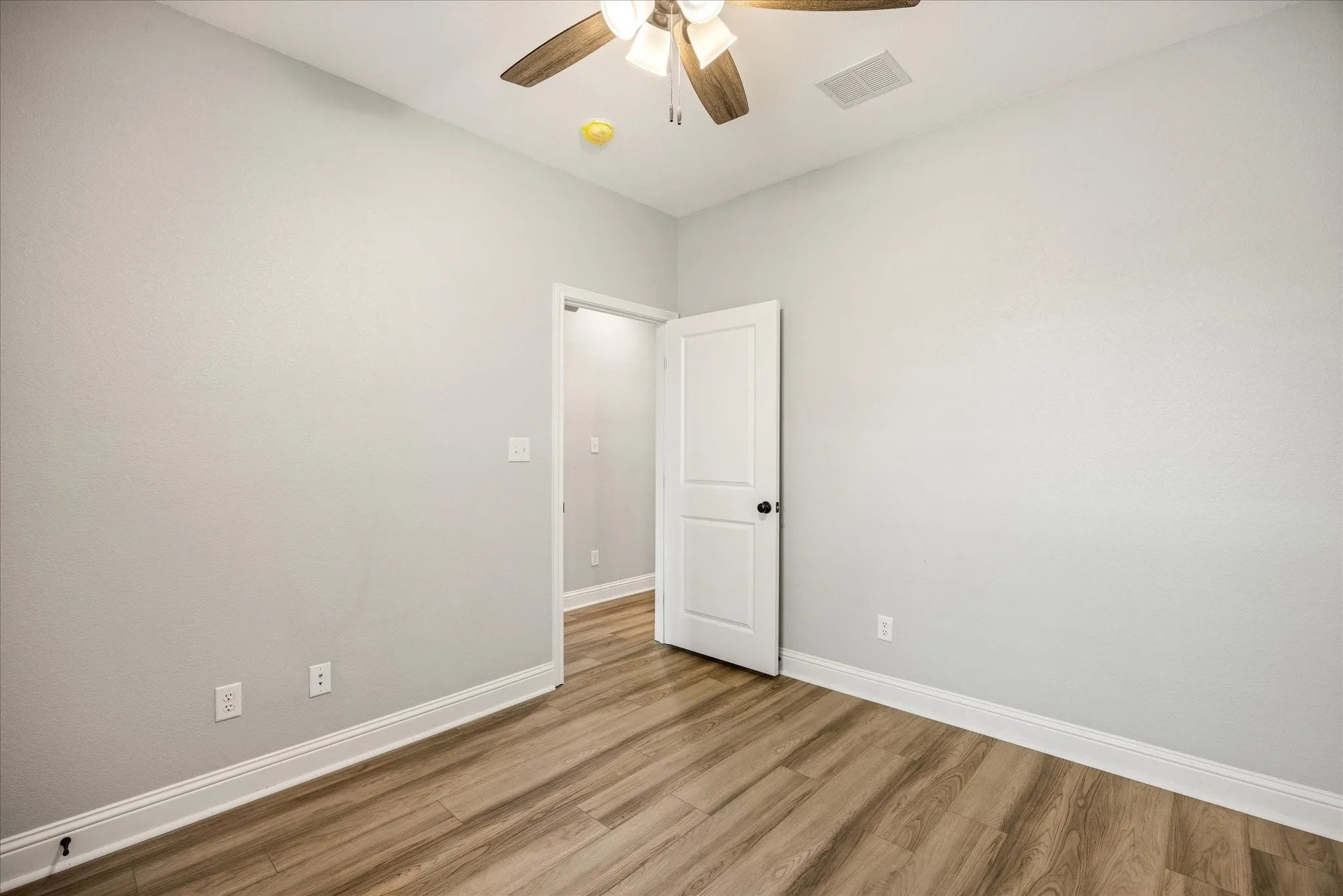 Interior room featuring light gray walls, wood-finish flooring, a ceiling fan with integrated lighting, and white baseboards
