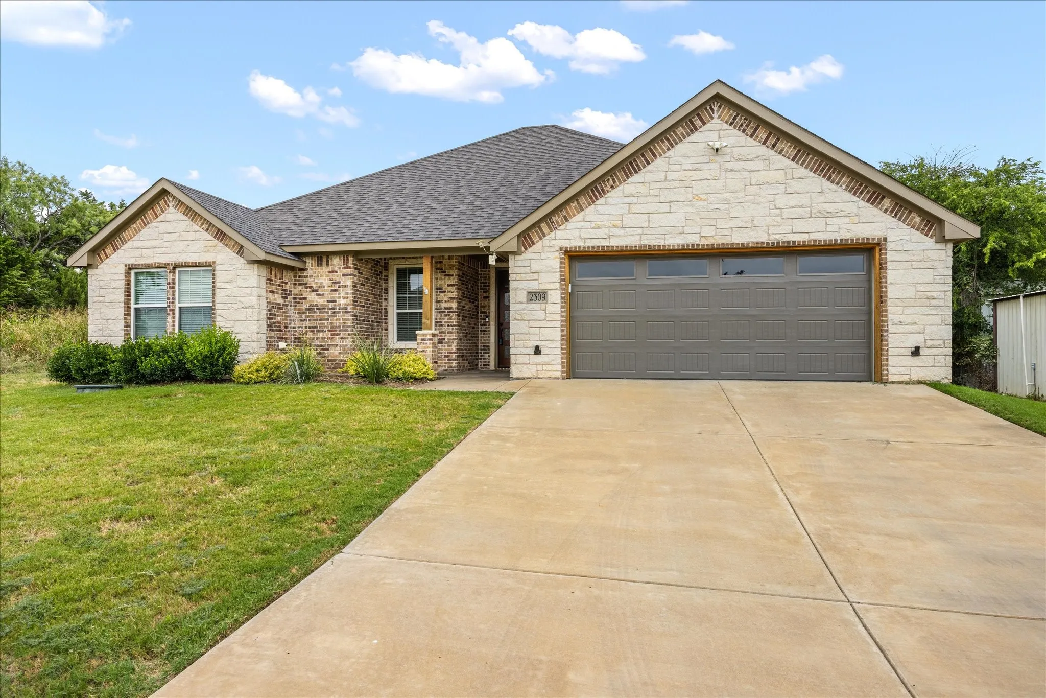 Exterior featuring a combination of brick and stone siding, an attached two-car garage with a panel door, a paved driveway, and a shingle roof