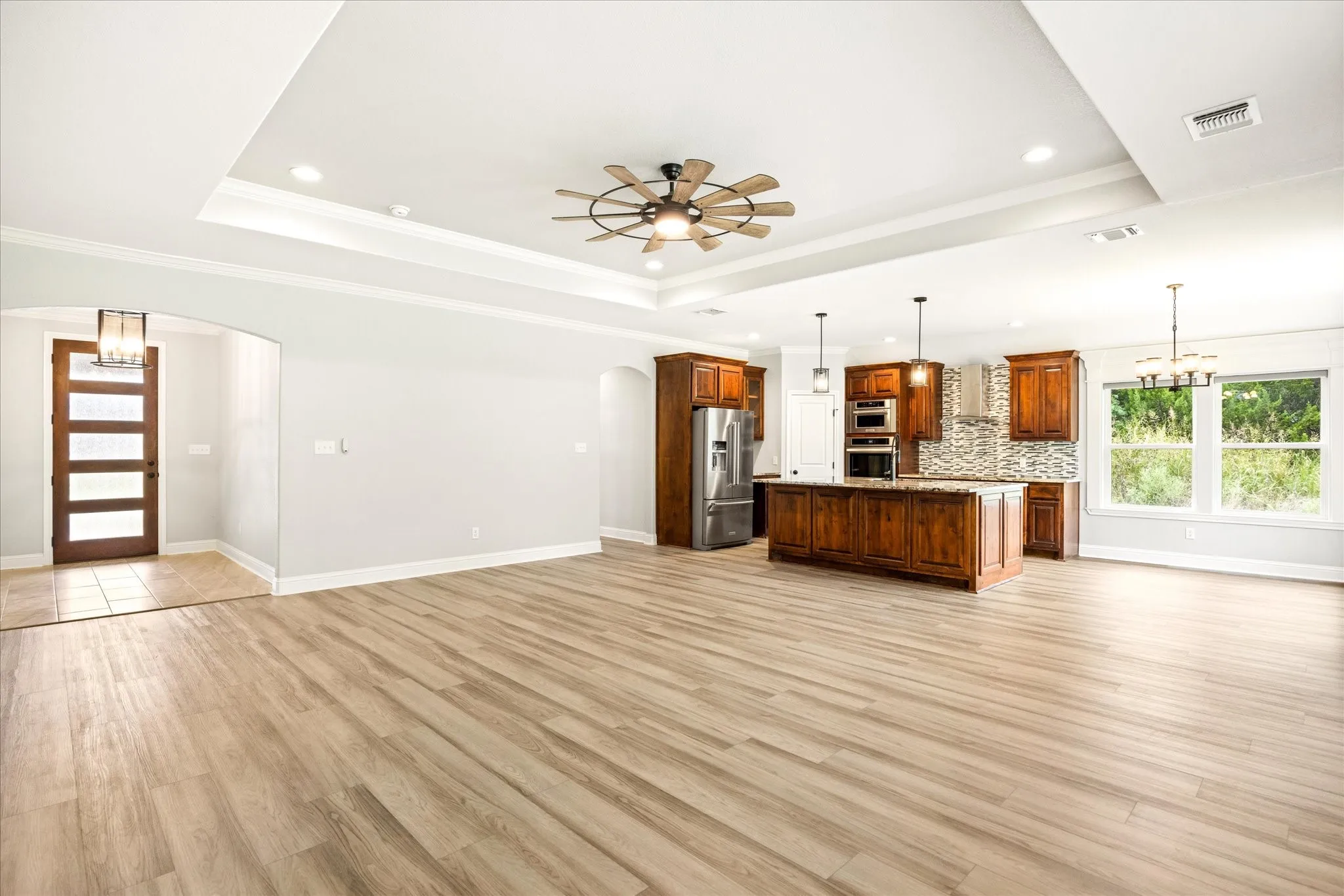 Spacious open concept interior featuring wood-finish flooring, a tray ceiling with recessed lighting, and a modern ceiling fan