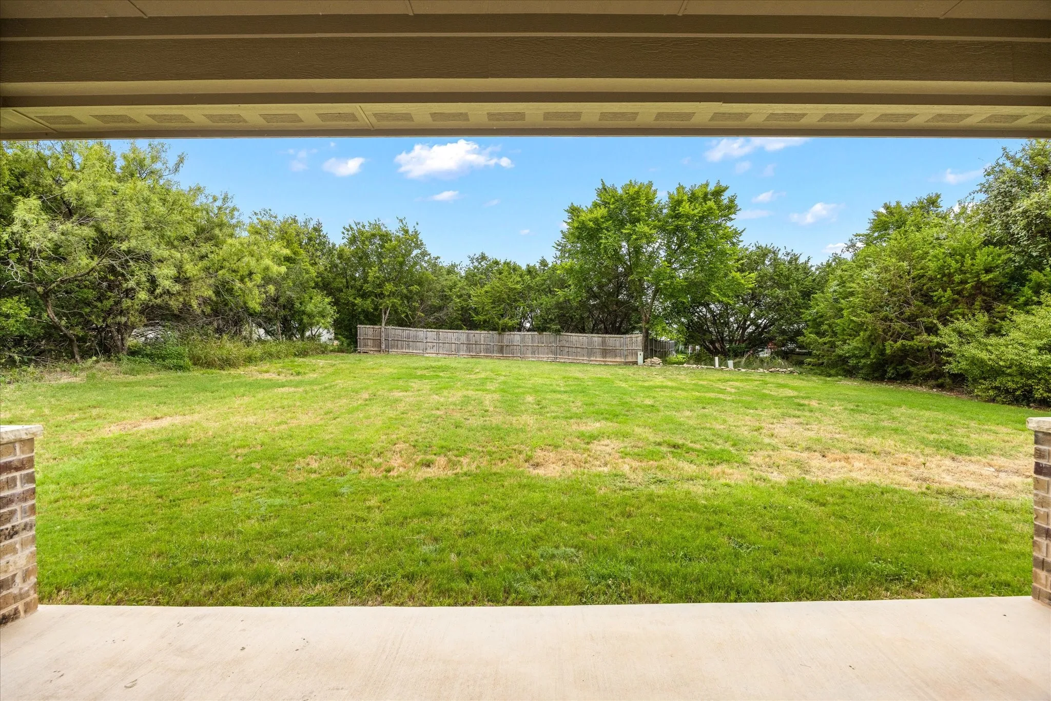 Expansive rear yard featuring green lawn, mature trees, and a wood privacy fence