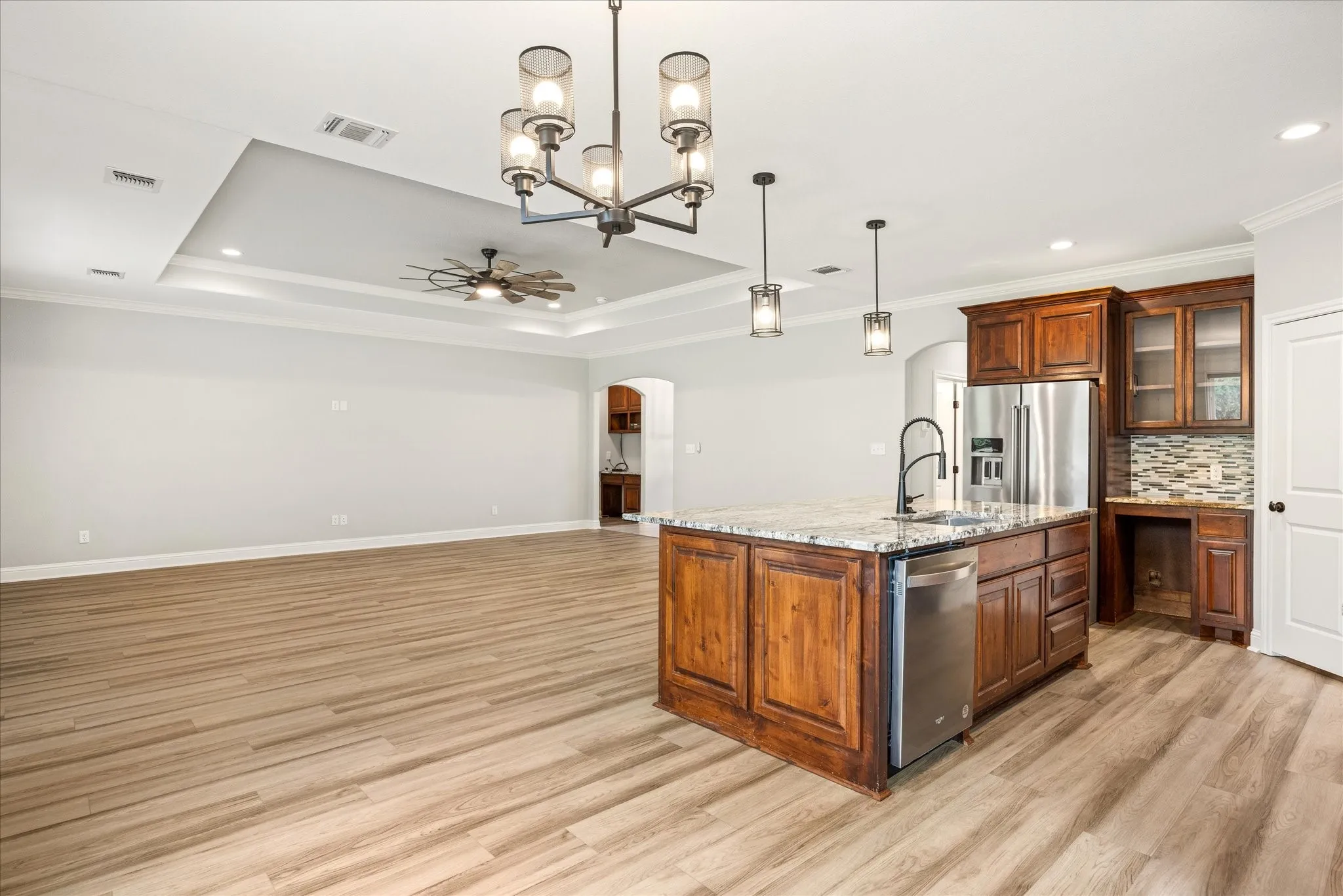 Open-concept living space featuring wood-finish flooring, a tray ceiling with recessed lighting and a ceiling fan, and a kitchen island with stone countertops