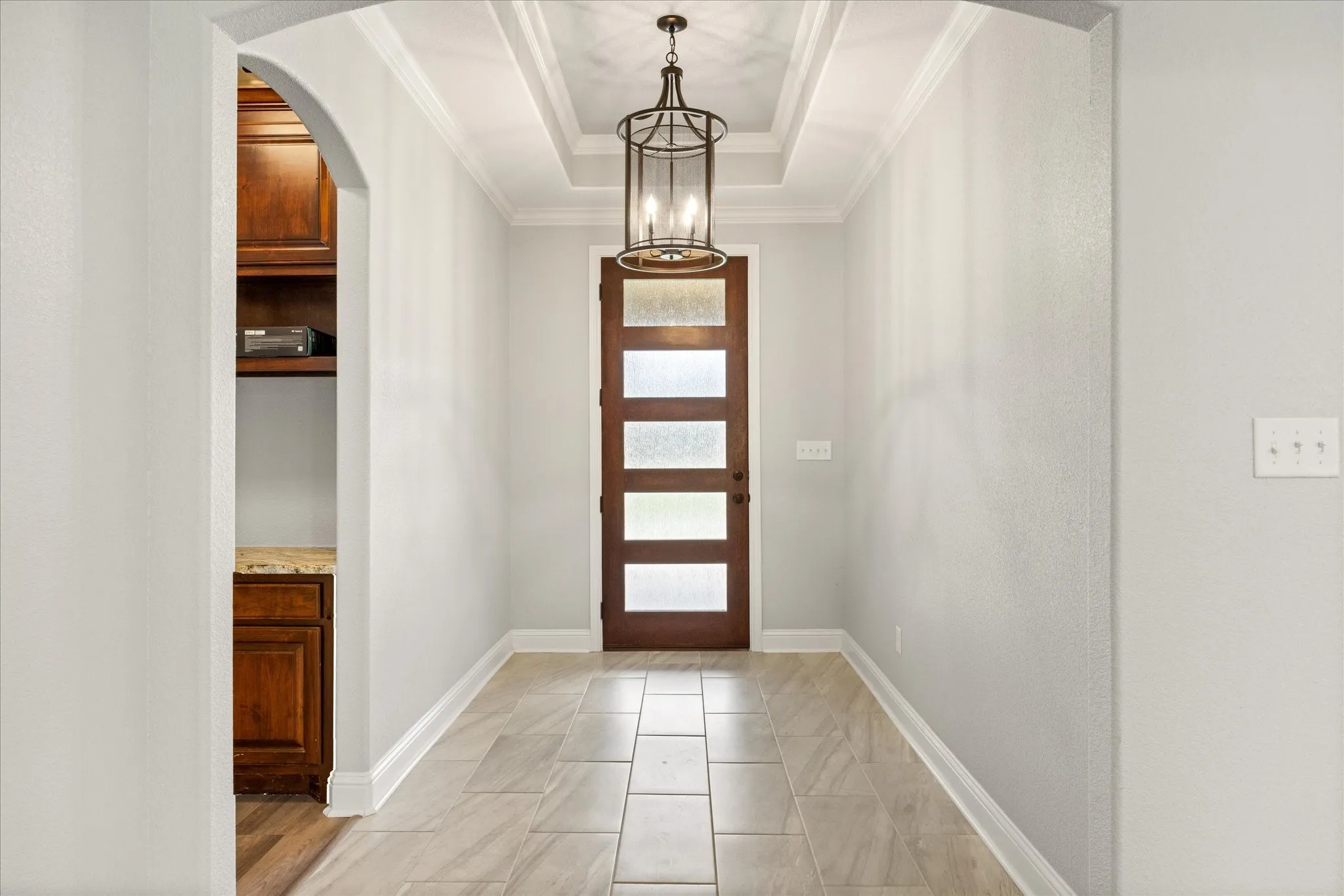 Entryway featuring a wood-panel door with privacy glass, an overhead light fixture, a coffered ceiling, and large format tile flooring