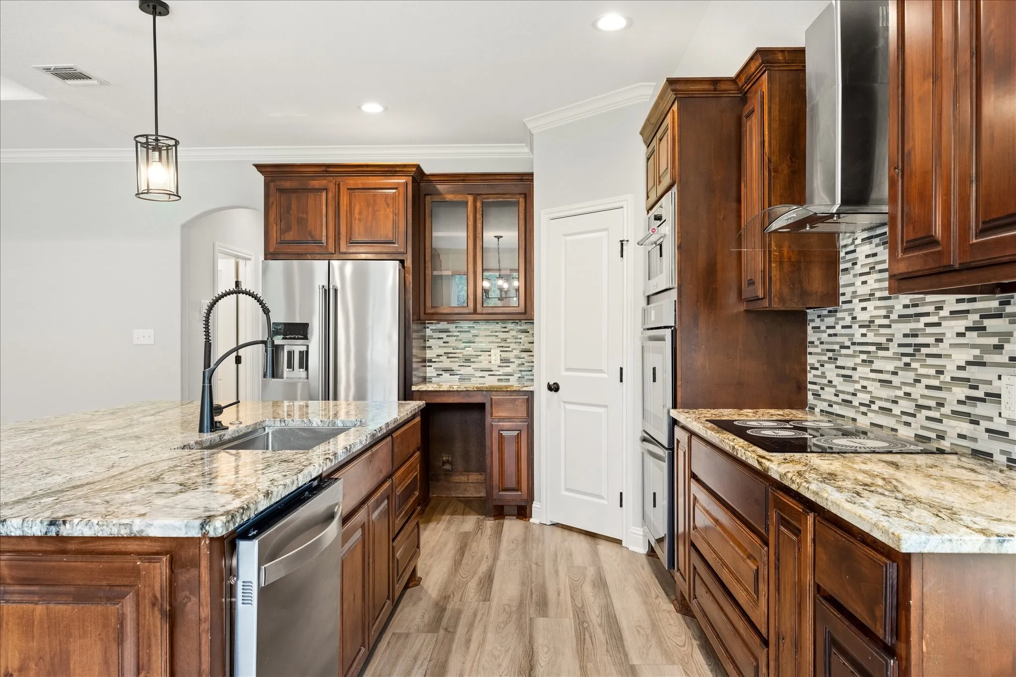 Gourmet kitchen featuring granite countertops, wood-finish flooring, stainless steel appliances, a built-in cooktop, and a tile backsplash