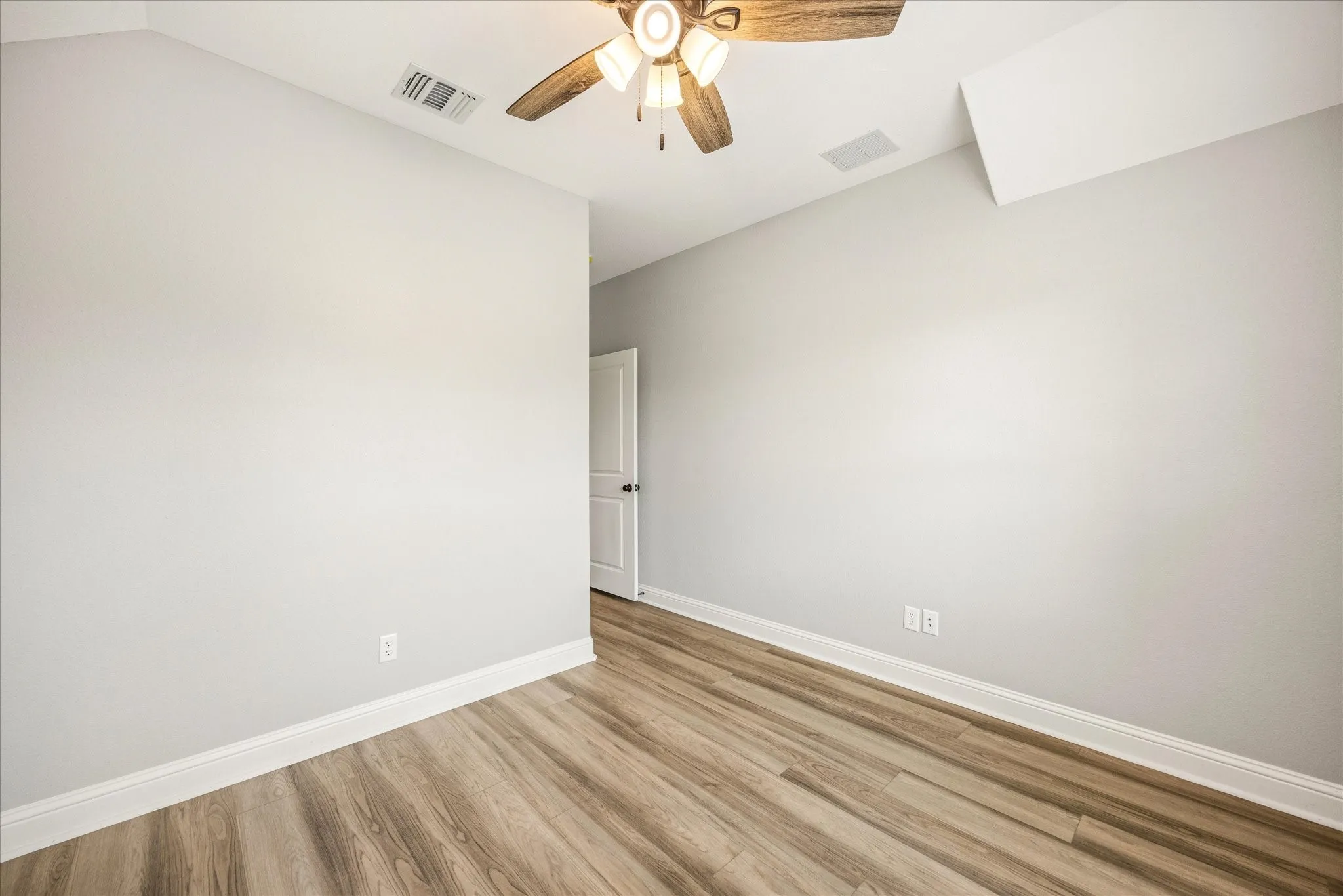 Room featuring wood-finish flooring, light grey painted walls, white baseboards, and a ceiling fan with integrated lighting