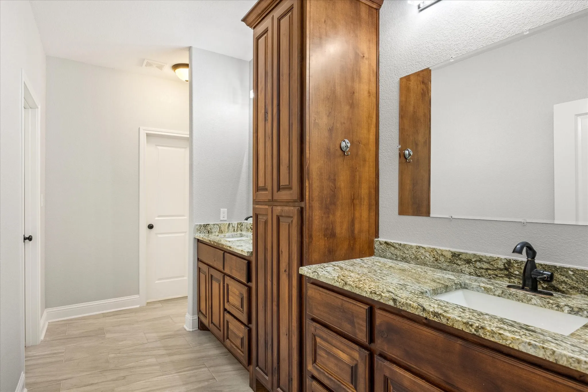 Dual vanity featuring wood-finish cabinetry, granite countertops, and integrated sinks