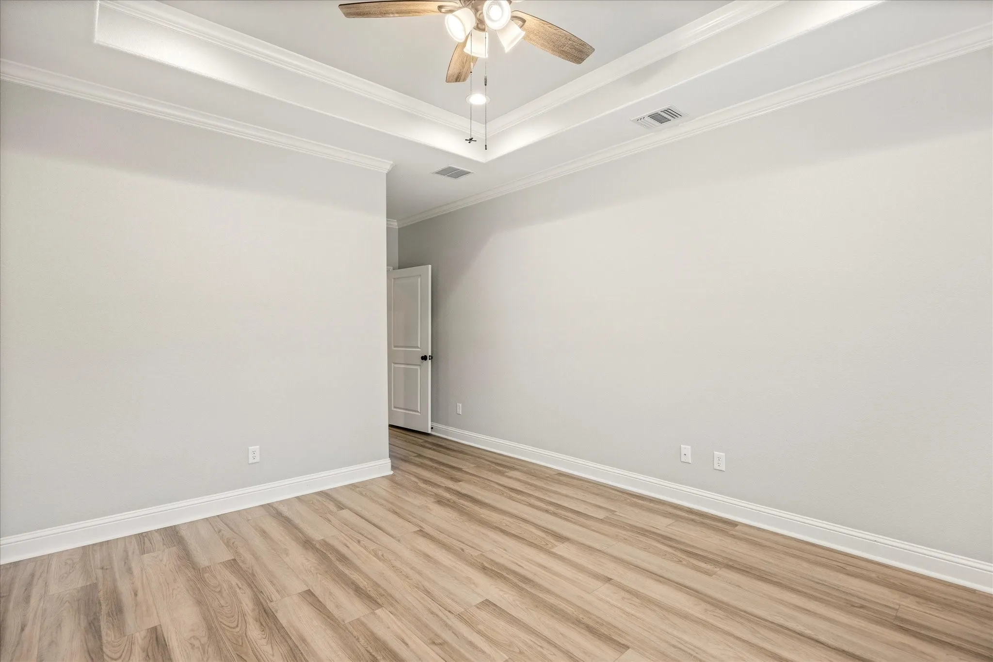 Spacious room featuring a tray ceiling with crown molding, a ceiling fan with integrated lighting, wood-finish flooring, and crisp white baseboards