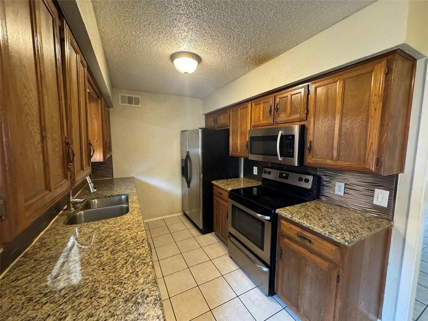 Kitchen featuring granite-style countertops, stainless steel appliances, wood cabinetry, a double basin sink, and tile flooring