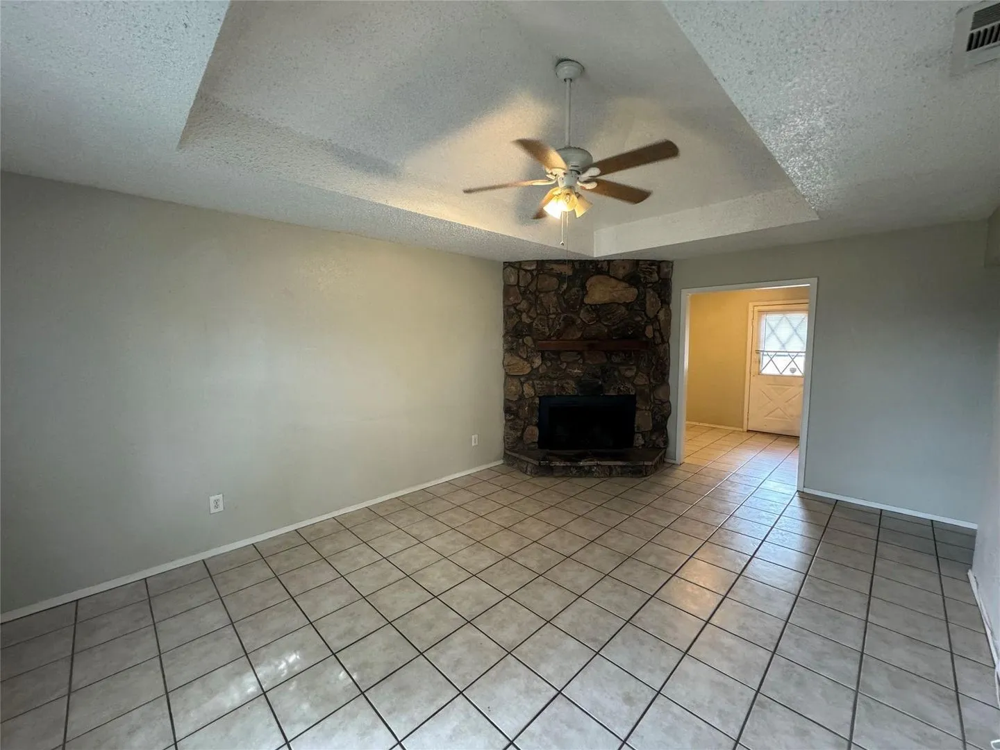 Living area featuring a corner stone fireplace with a wood mantle, tray ceiling, ceiling fan, and ceramic tile flooring